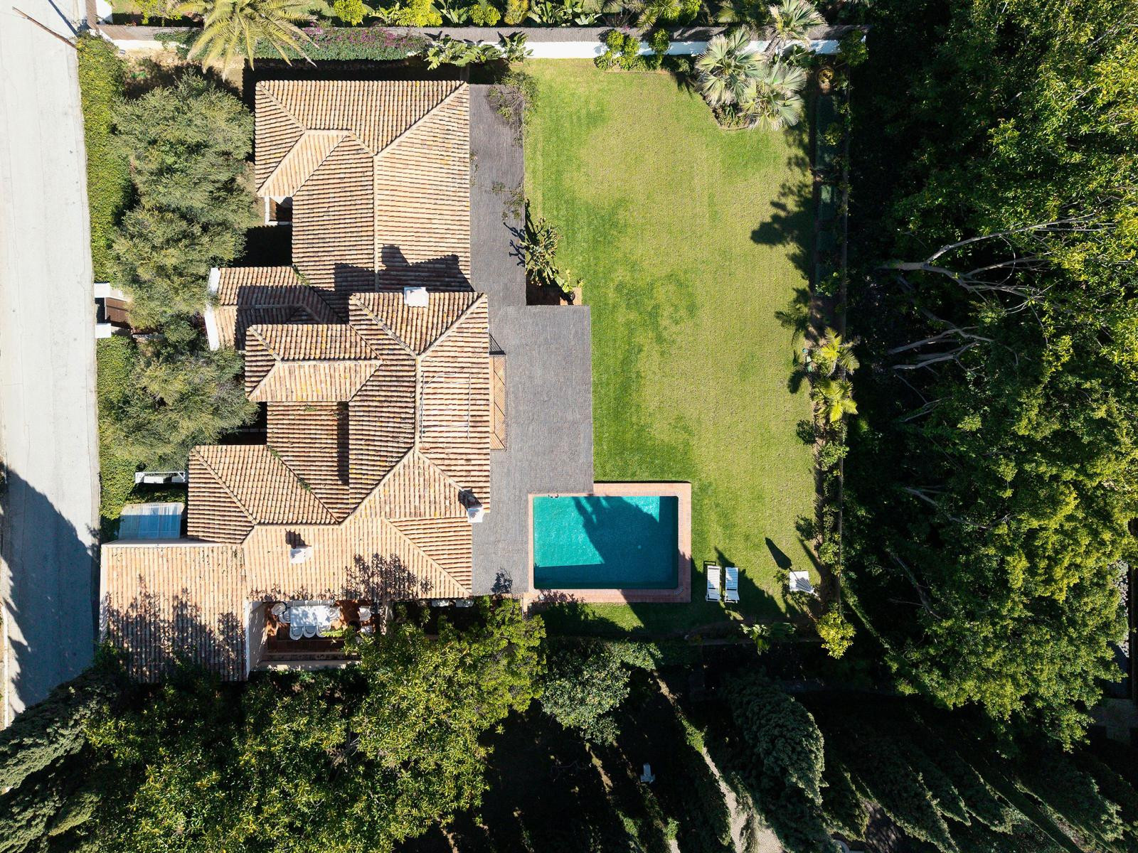 Aerial view of a property with terracotta tiled roofs, a rectangular pool, and extensive green landscaping.