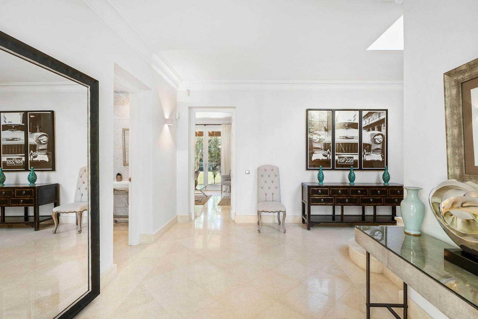 Entrance hallway with marble floors, a large mirror, console tables, and an open doorway to another room.
