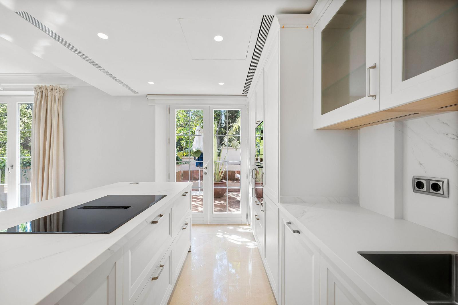 Kitchen aisle with an induction cooktop on the island, white cabinets, and double doors to a patio.