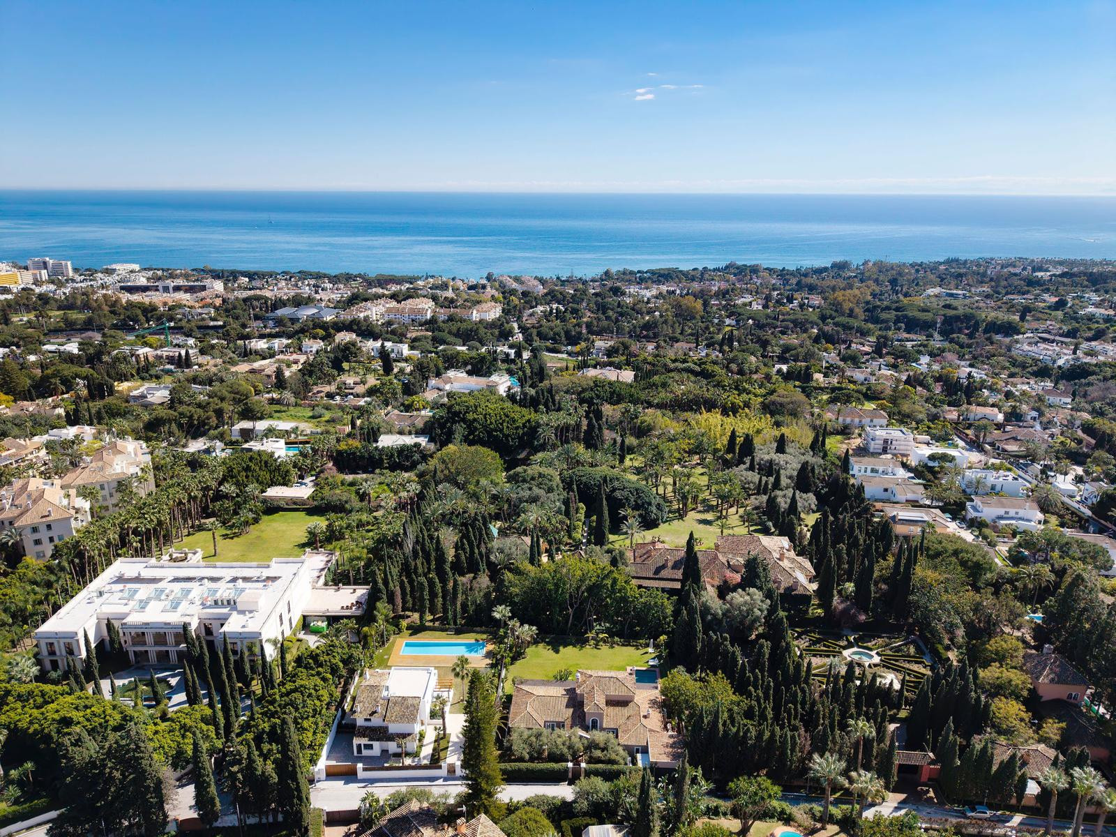 Aerial view of multiple luxury villas, lush green landscaping, and the Mediterranean Sea under a clear blue sky.