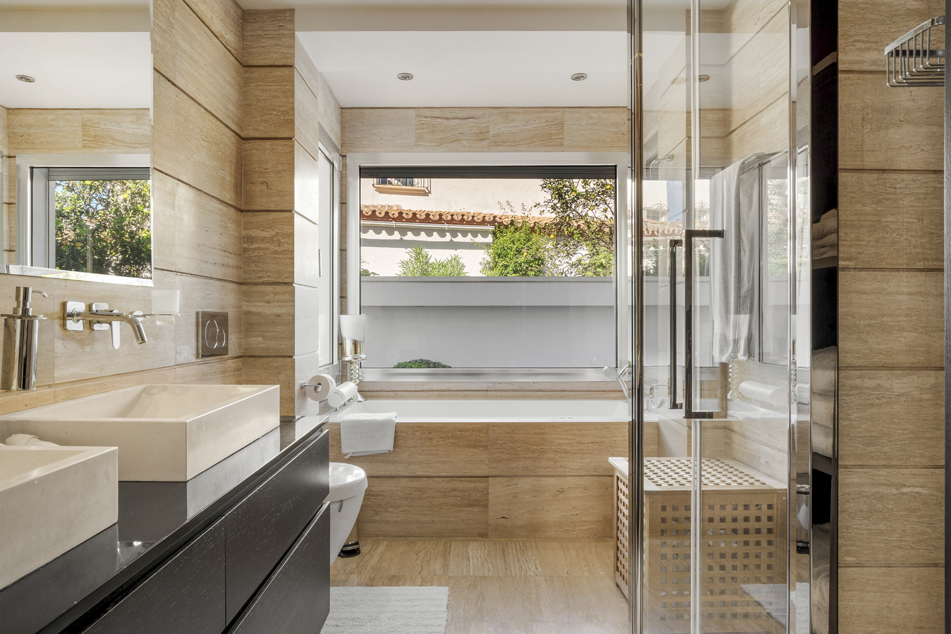 Modern bathroom with double vanity, walk-in shower, bathtub under a window, and wood-effect tiling.