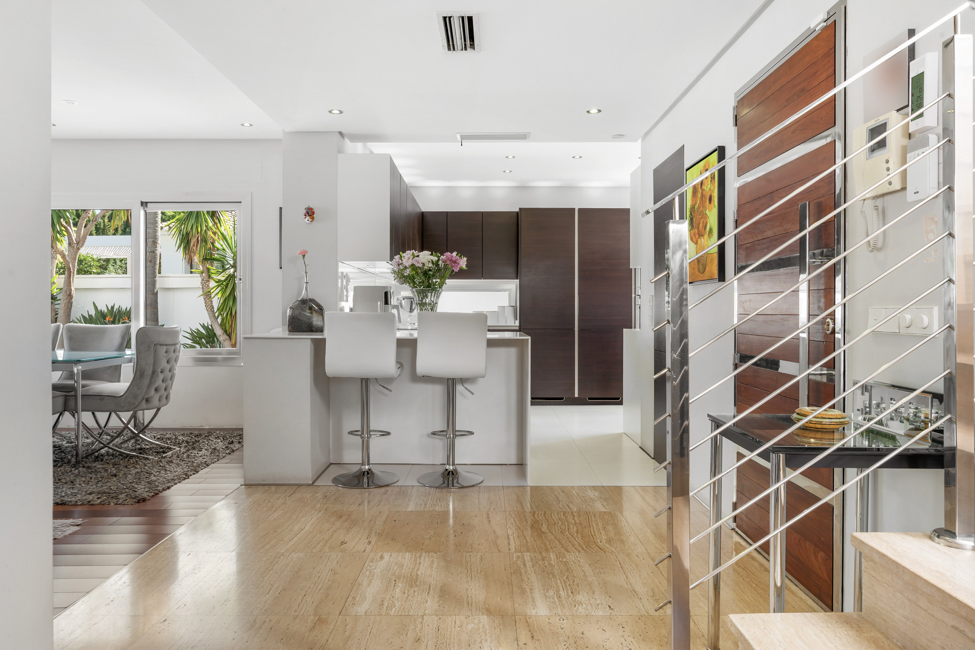 Open plan kitchen and dining area with white bar stools, dark wood cabinetry, and marble flooring.