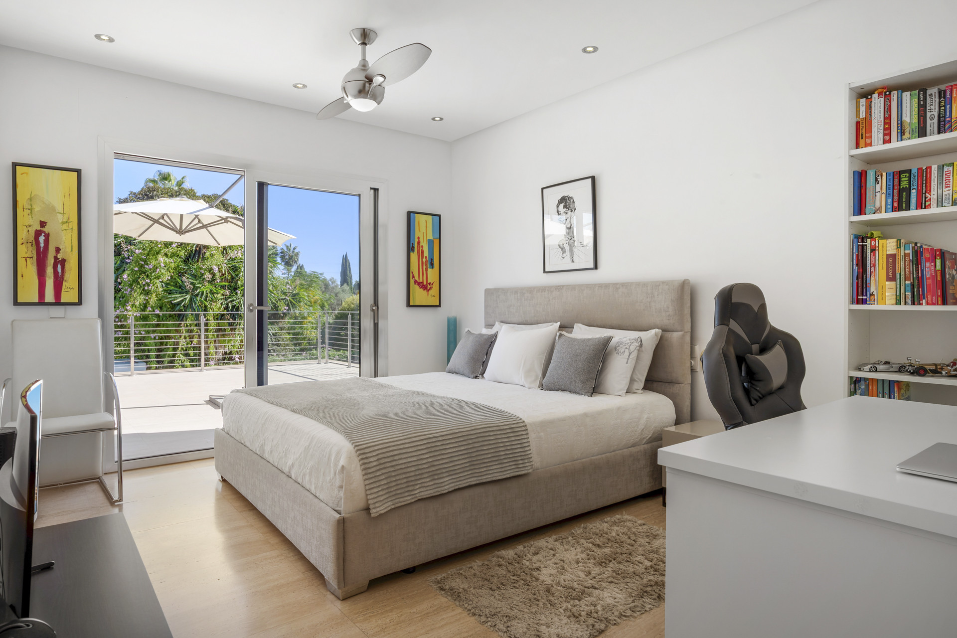 Bedroom with a large gray bed, white bedding, open glass doors to a balcony, and a ceiling fan.
