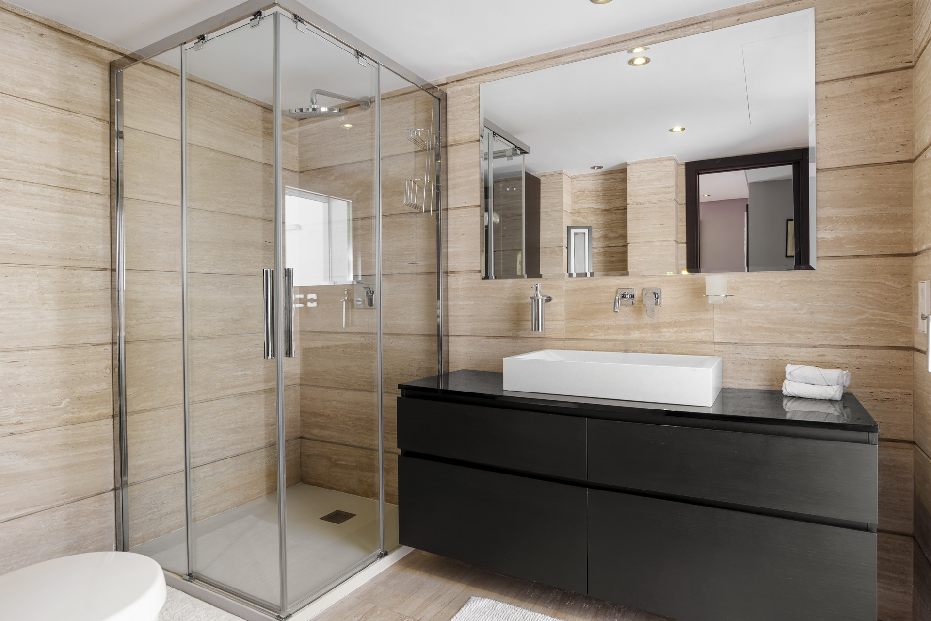 Bathroom with a glass walk-in shower on the left and a large dark vanity with a white rectangular sink.