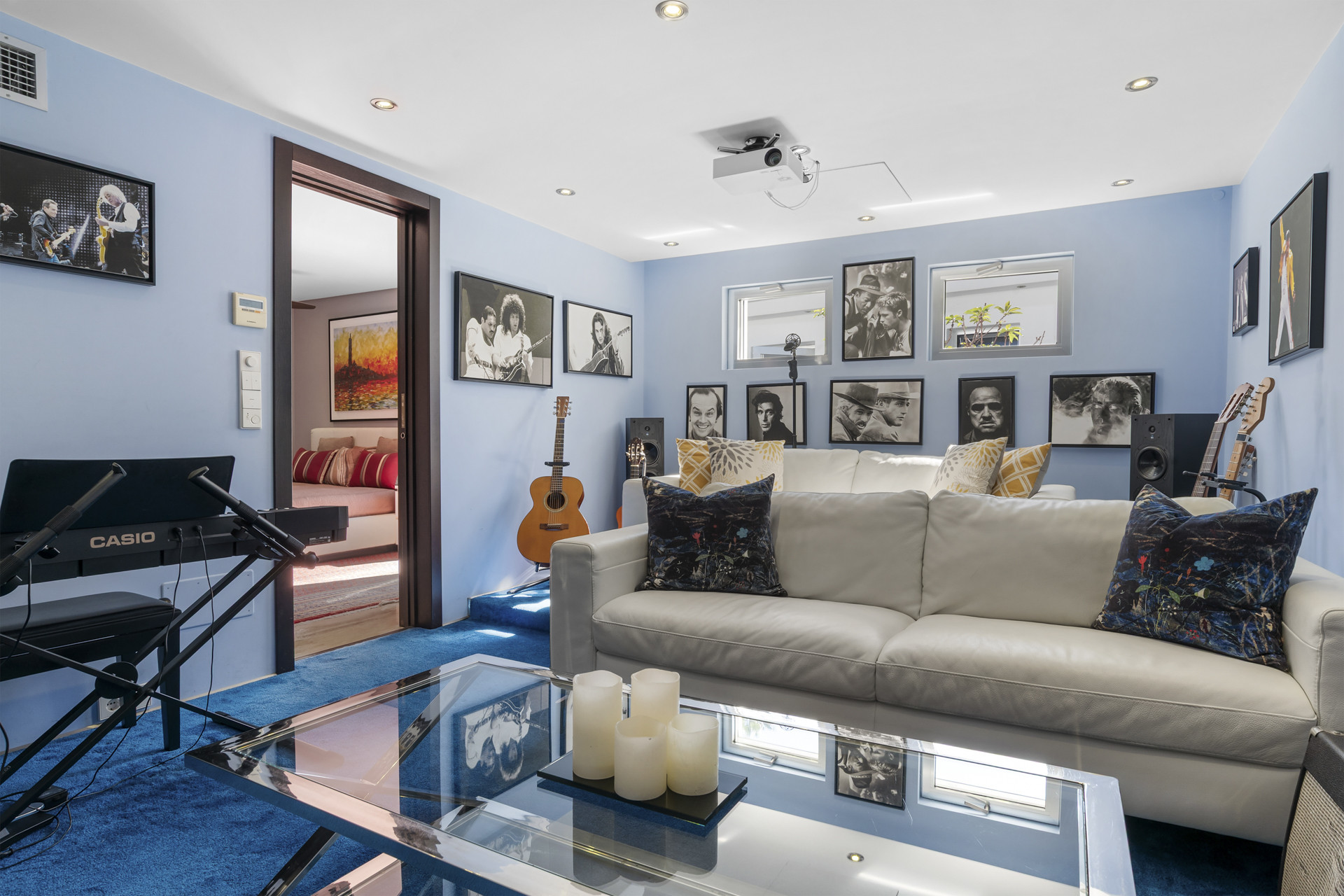 A bright blue music room with white sofas, a projector, framed celebrity photos, and a keyboard.
