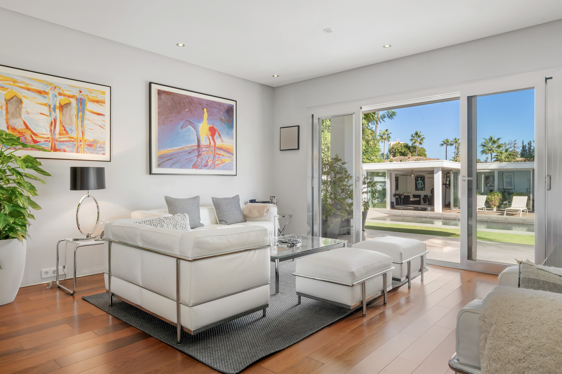 Living room with white furnishings, sliding glass doors opening to a pool and lounge area.
