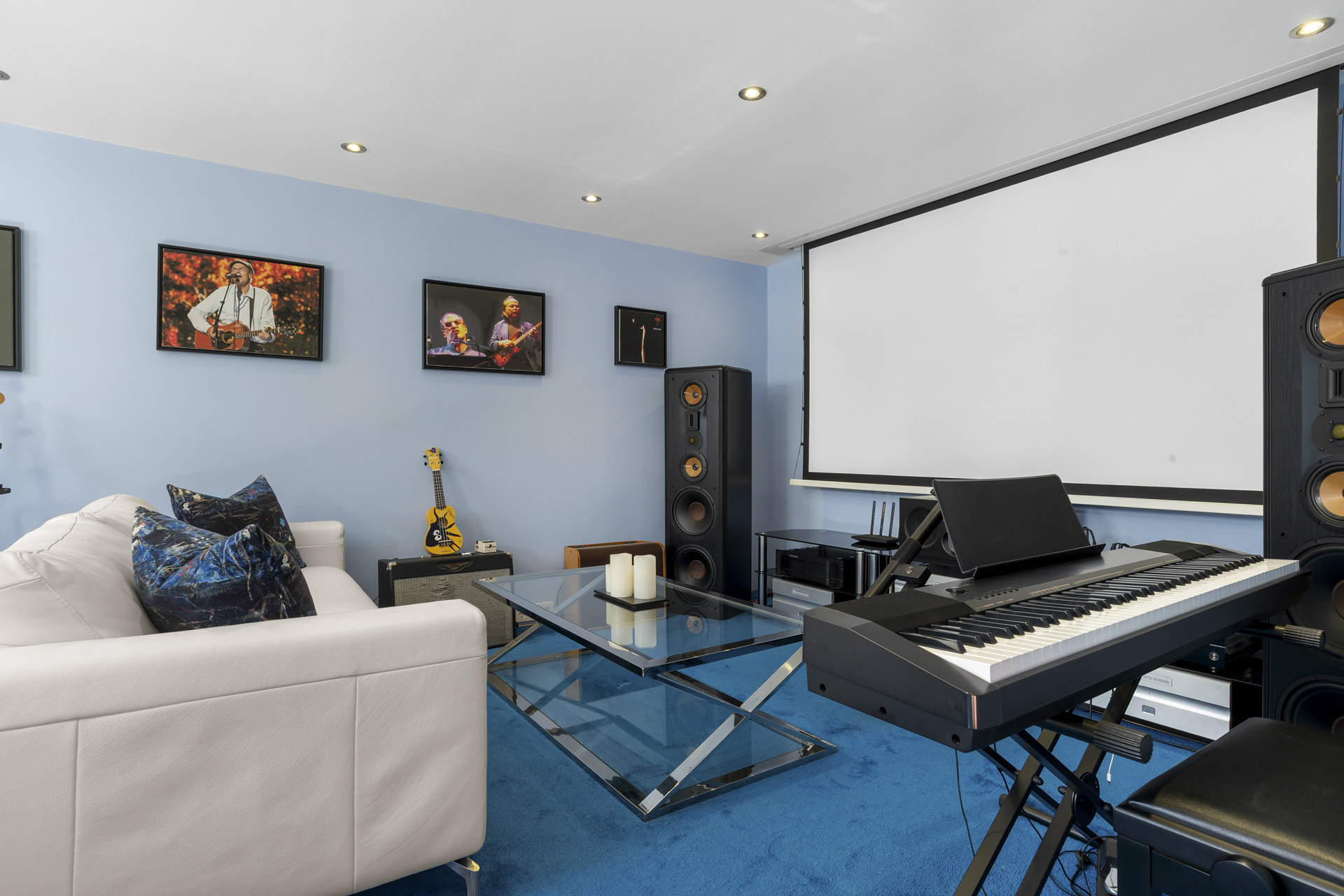 Media room with a projection screen, blue carpet, a white sofa, and musical instruments.