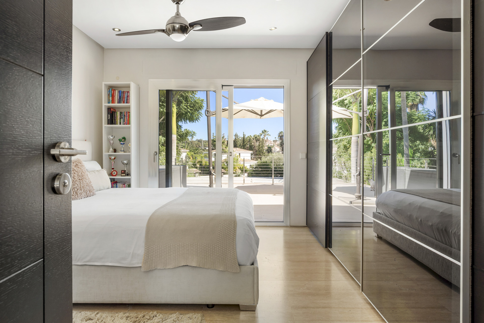 Bedroom with a large bed, ceiling fan, mirrored closet doors, and sliding door to a balcony.