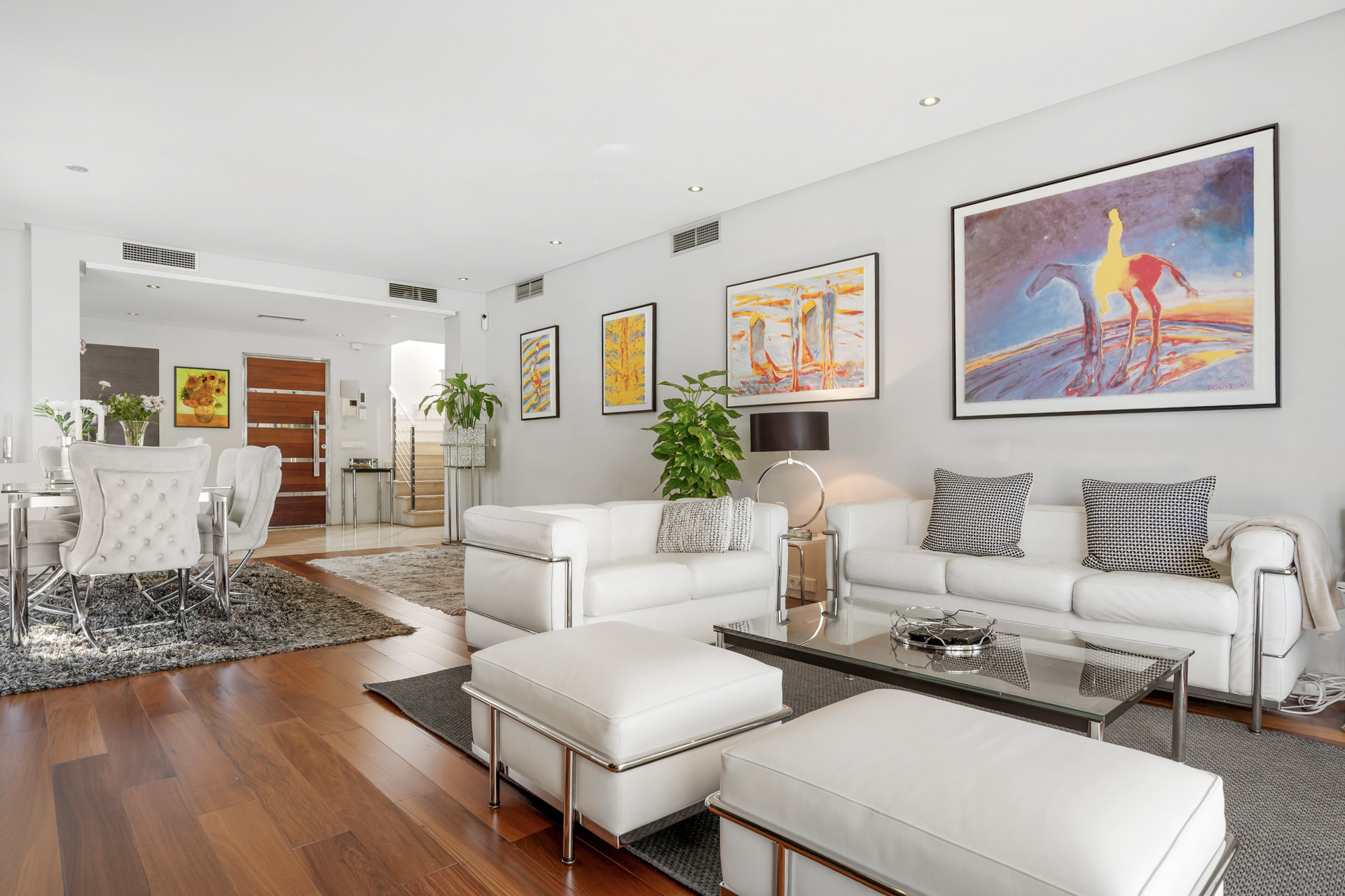 Modern living room with white sofas and colorful art, looking into the dining area.