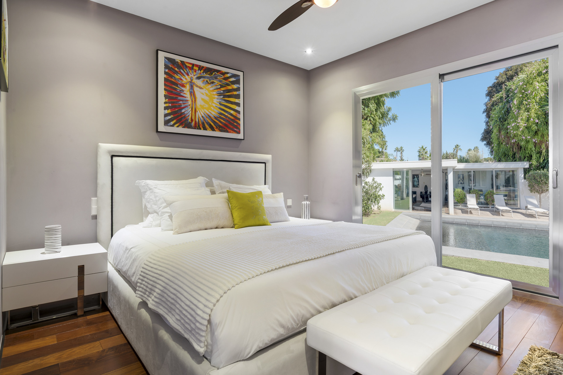 Bedroom with a white bed, lime green pillow, and sliding glass door to a pool area.