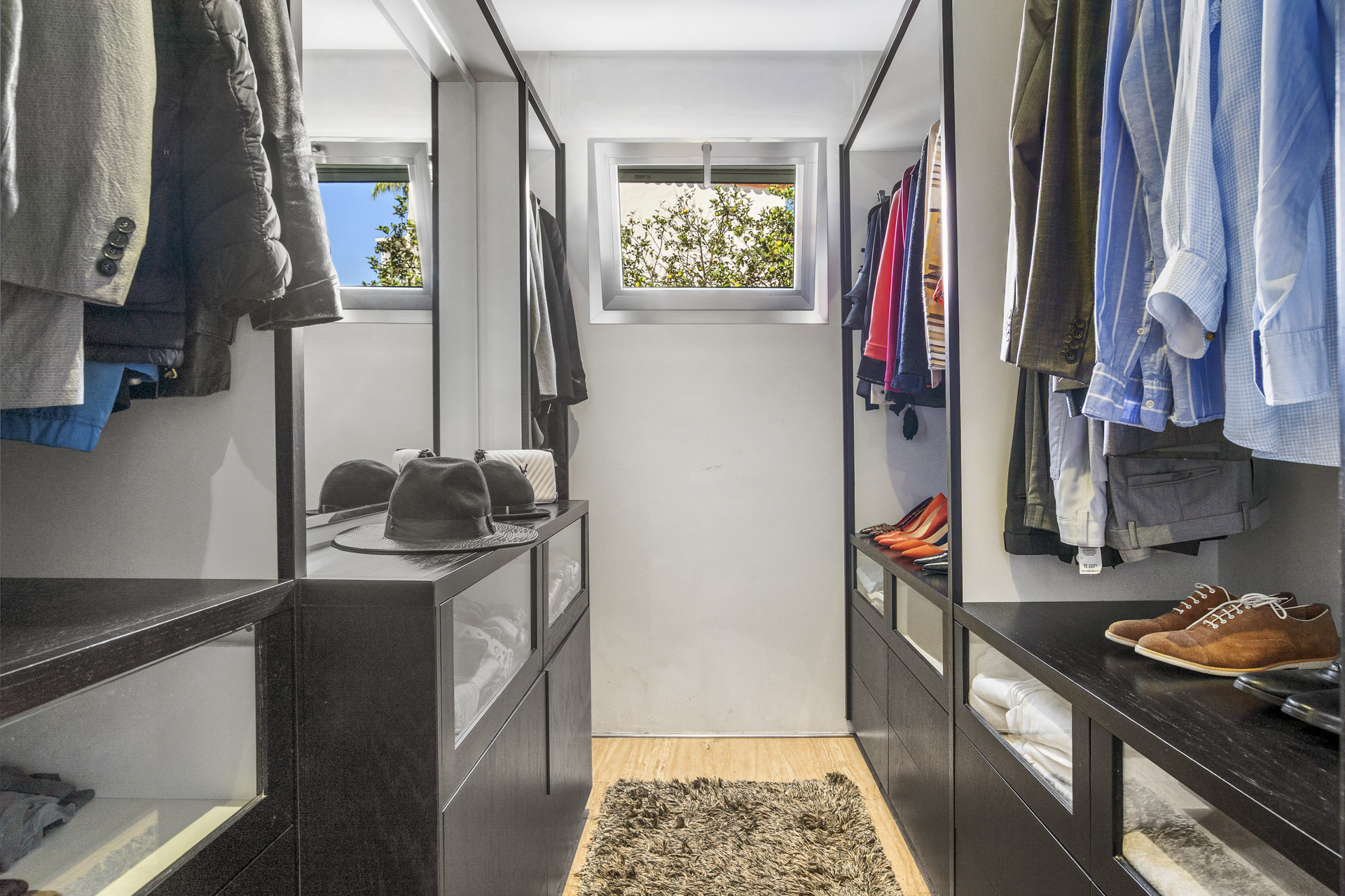 Walk-in closet with dark wood cabinetry, clothes racks, and a small window.