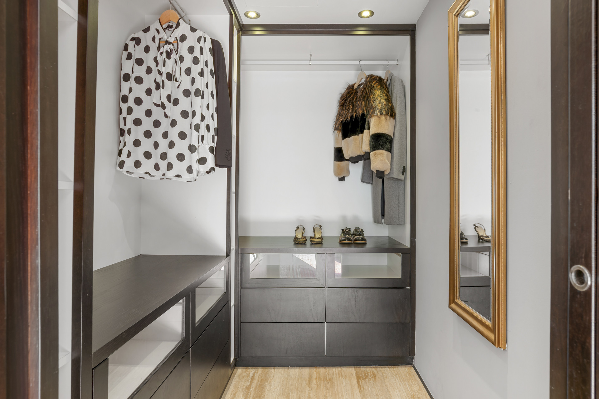 Walk-in closet with dark wood shelving, hanging clothes, and a floor-length mirror.