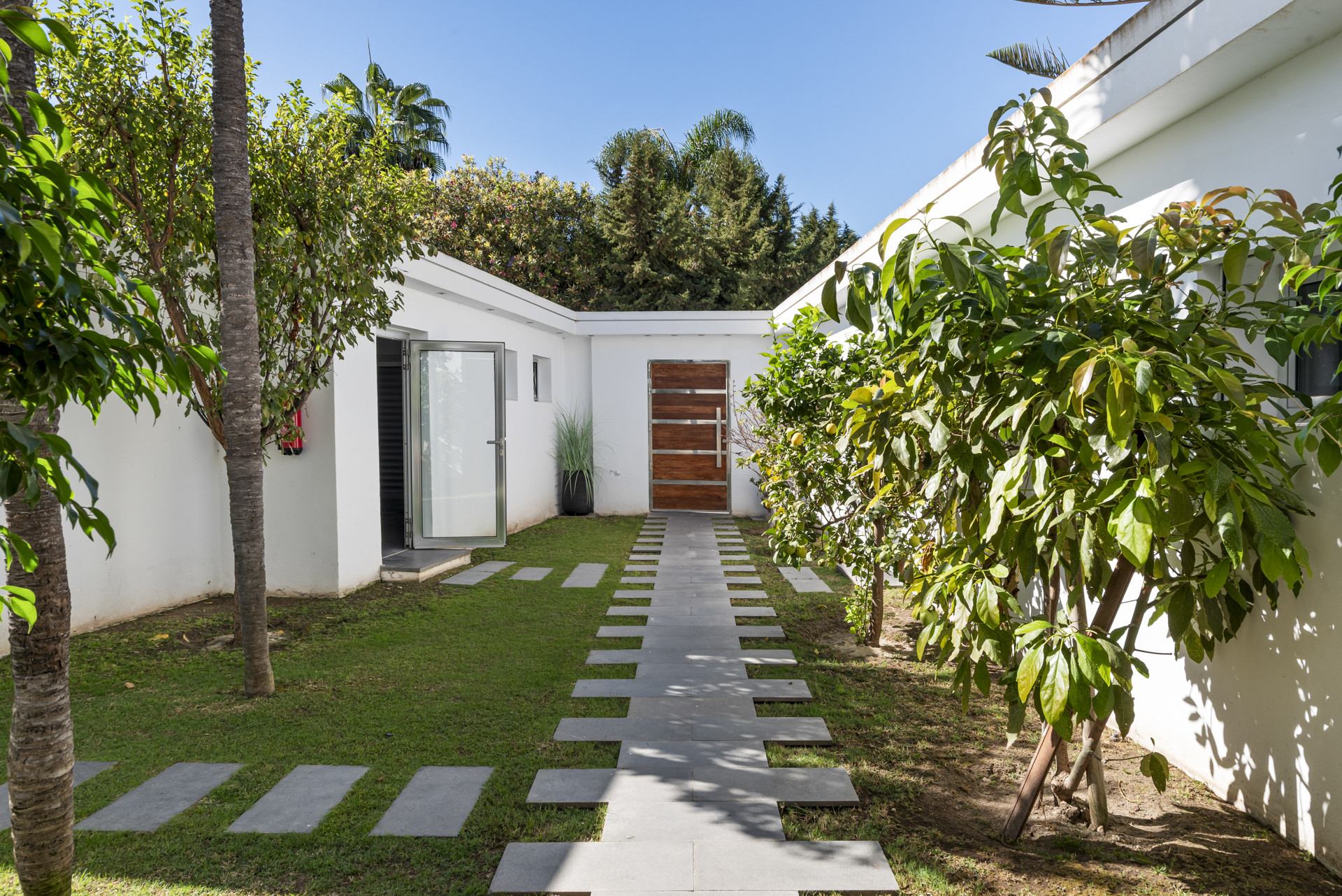 An outdoor path of grey stepping stones through green grass leading to a wooden front door.