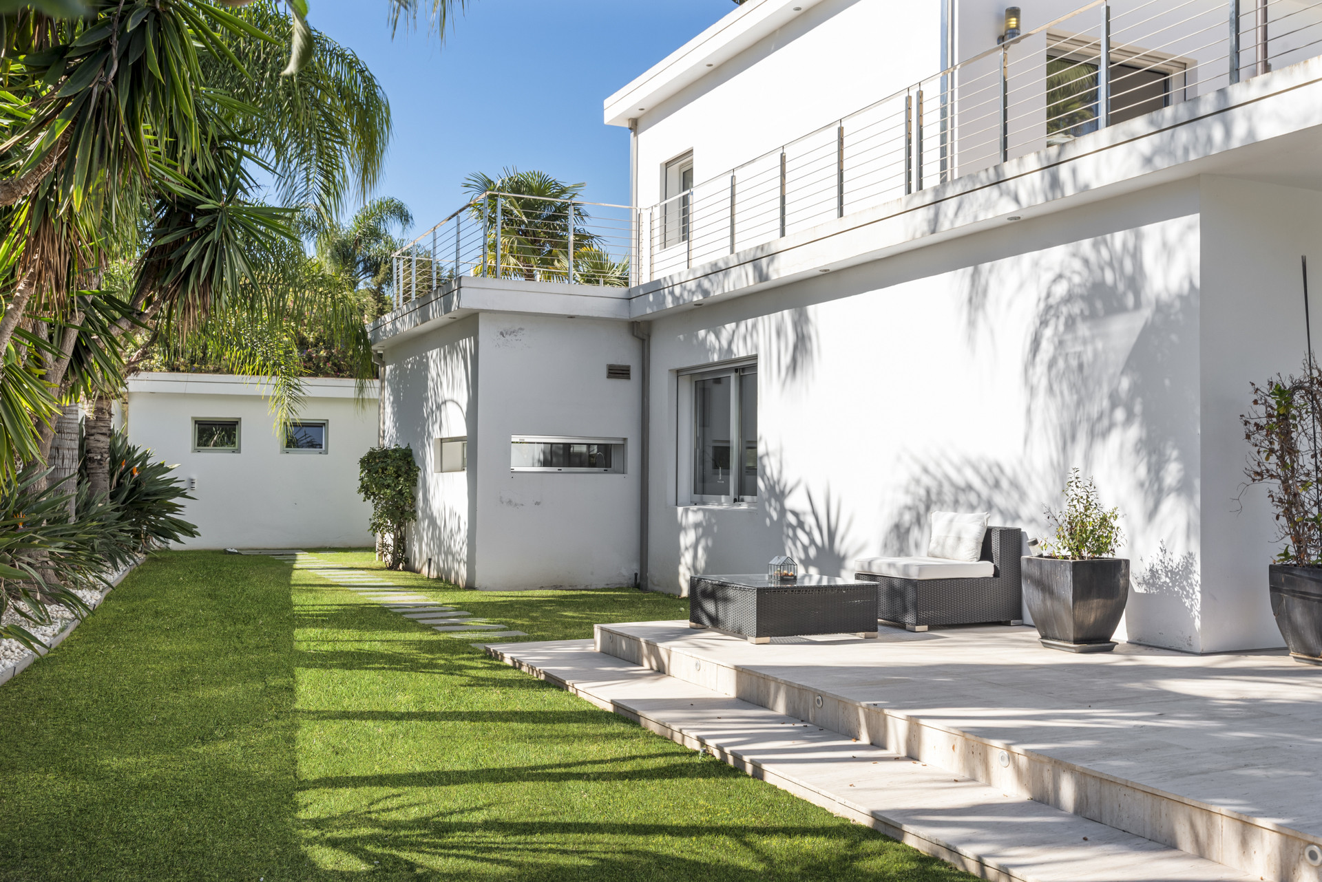 Exterior of a white modern villa with an artificial grass lawn and outdoor seating on a tiled patio.