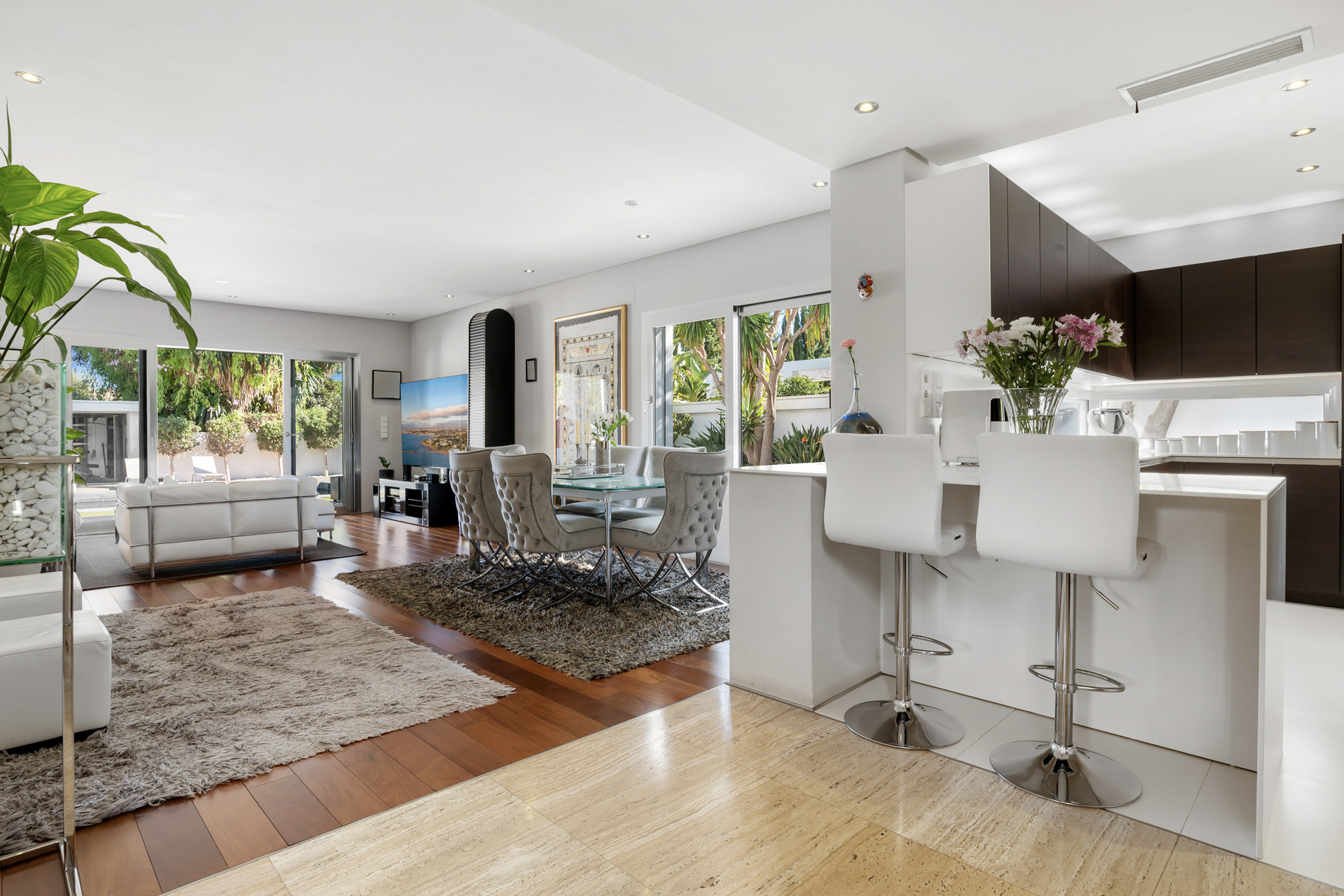 Open plan living area with an island kitchen bar, dining table, and a white sofa facing an outdoor patio.
