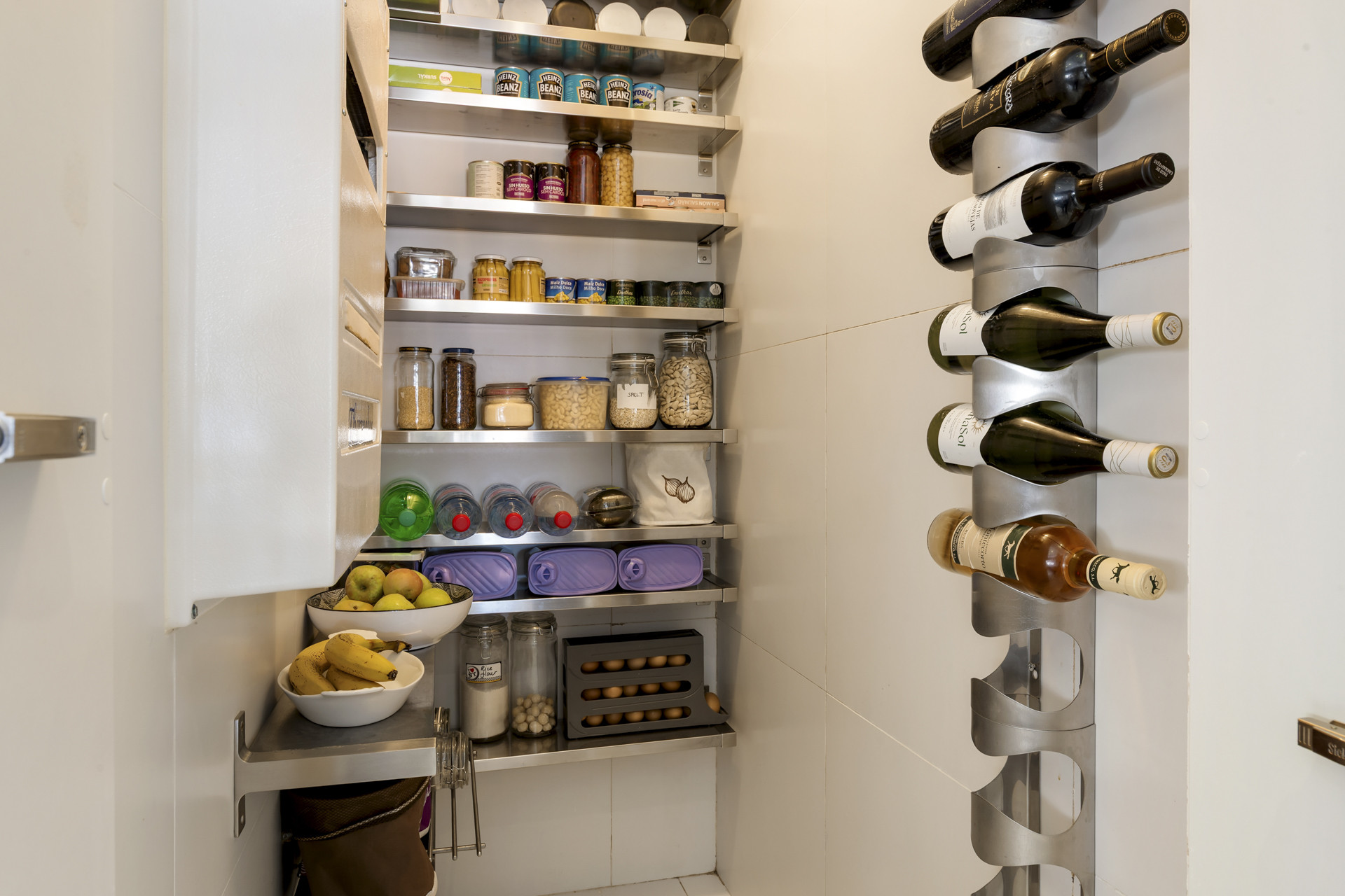 Walk-in pantry filled with shelves of food items and a wall-mounted wine rack with bottles.