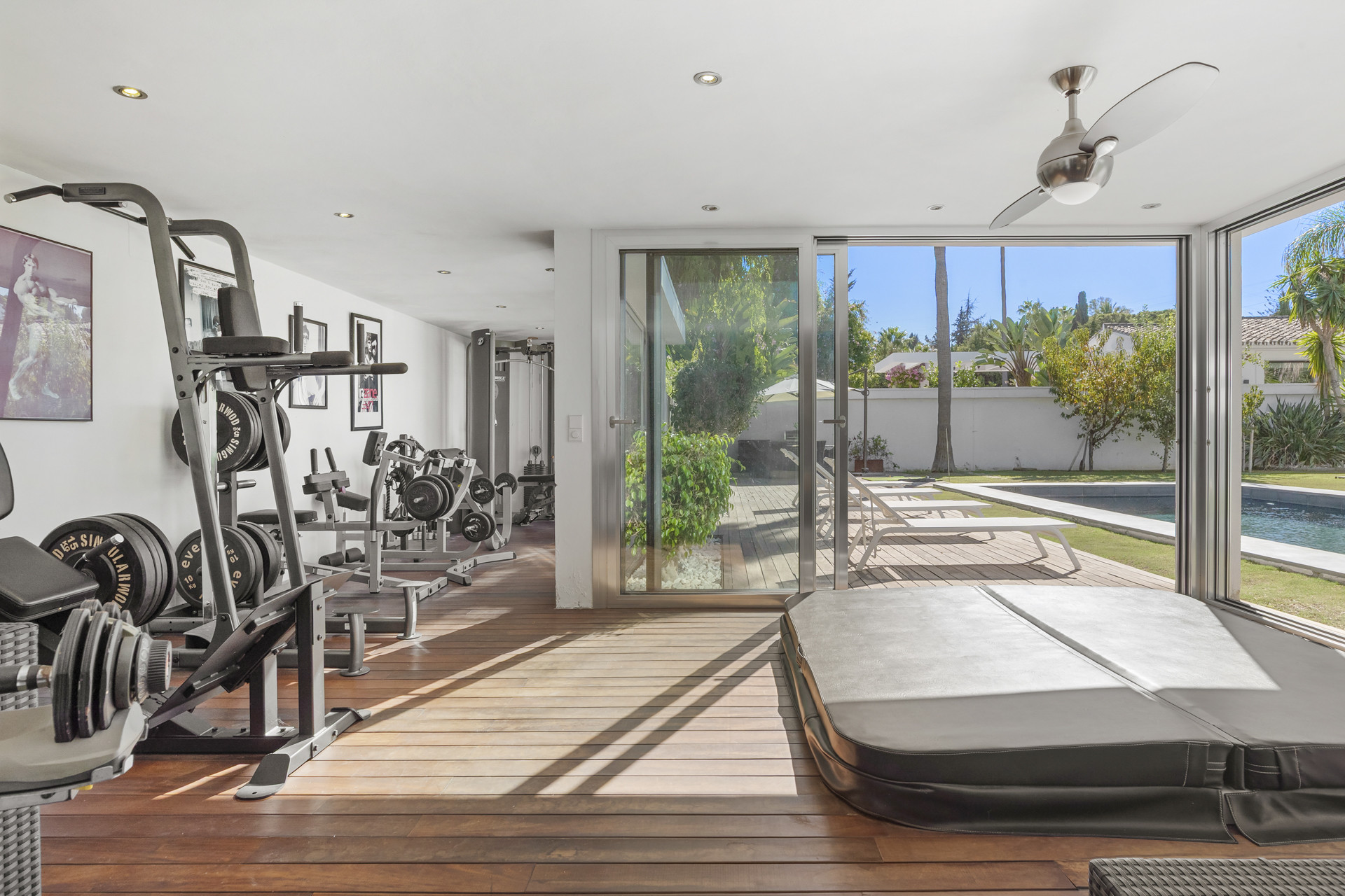 Indoor gym with weights, exercise machines, and a covered hot tub, open to a patio and pool area.