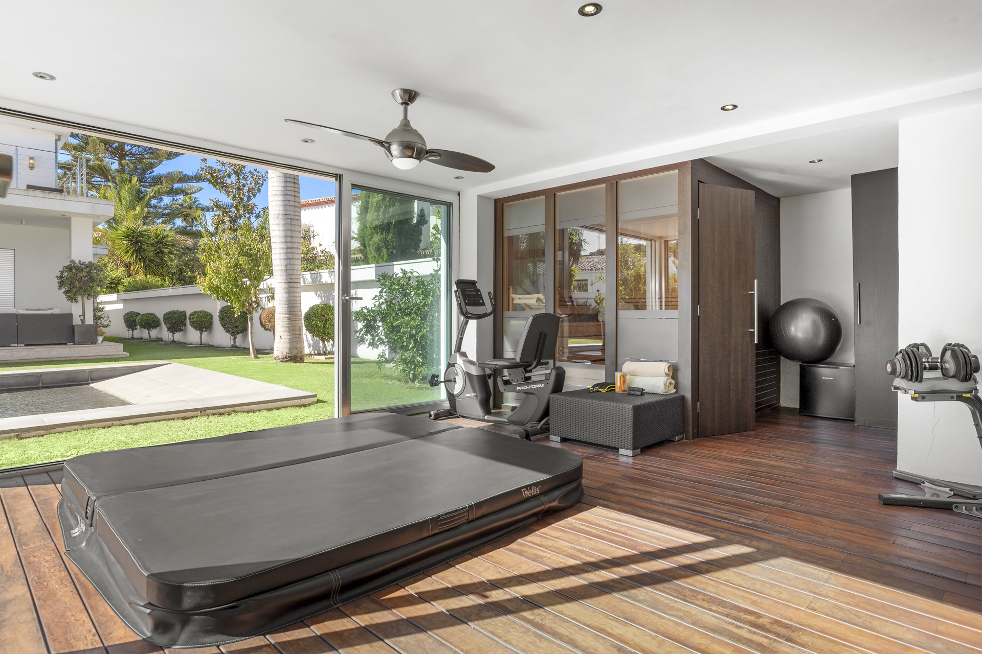 Indoor gym with hot tub, fitness equipment, and large sliding glass doors opening to a garden and pool.