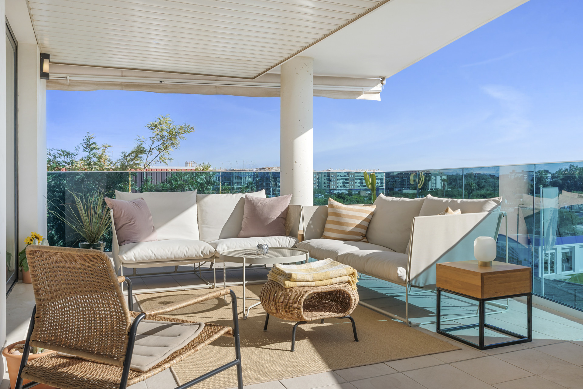 Covered outdoor balcony with two white sofas, a coffee table, and a wicker chair under clear sky.