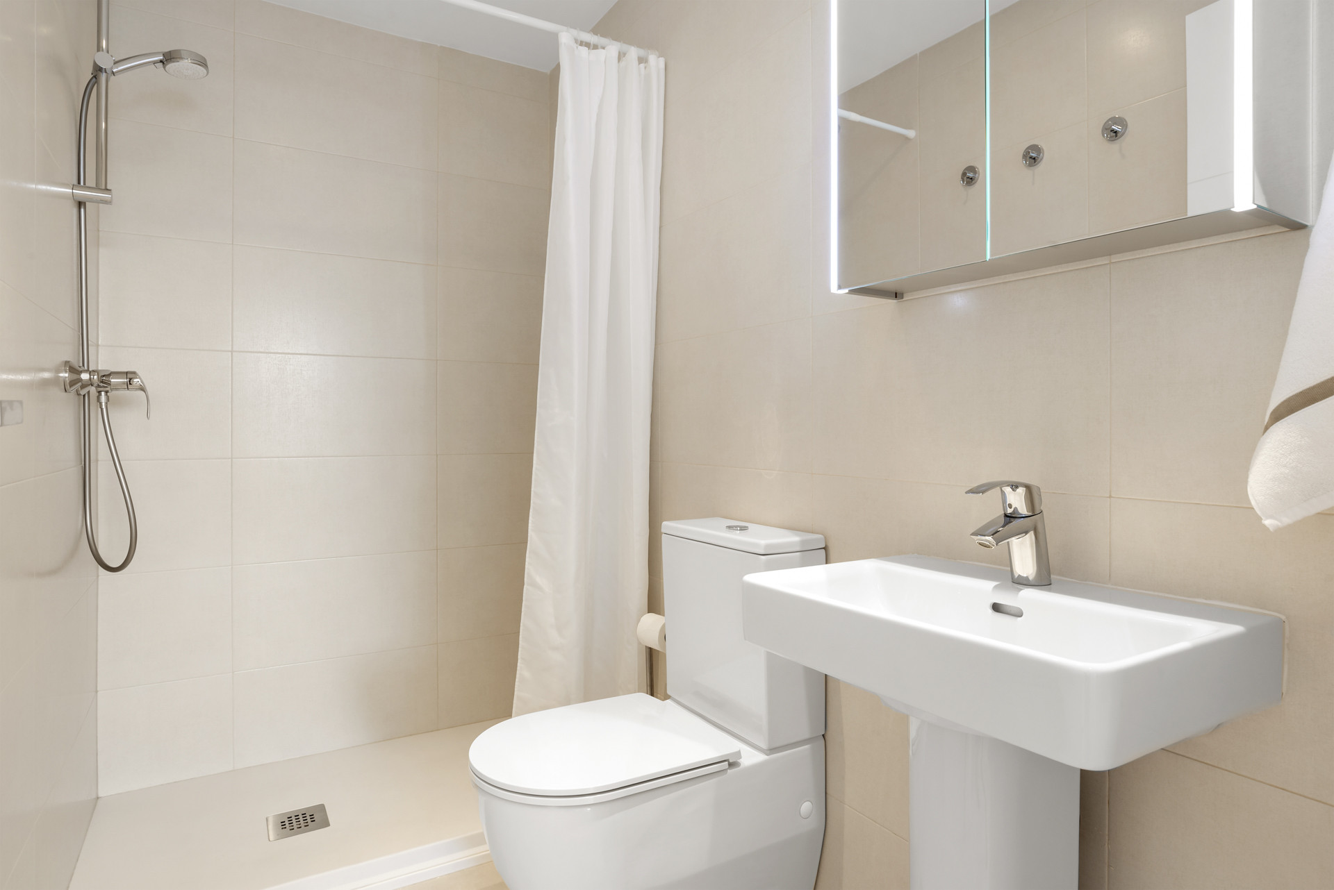 Bathroom with tiled walls, shower, toilet, pedestal sink, and illuminated mirror.