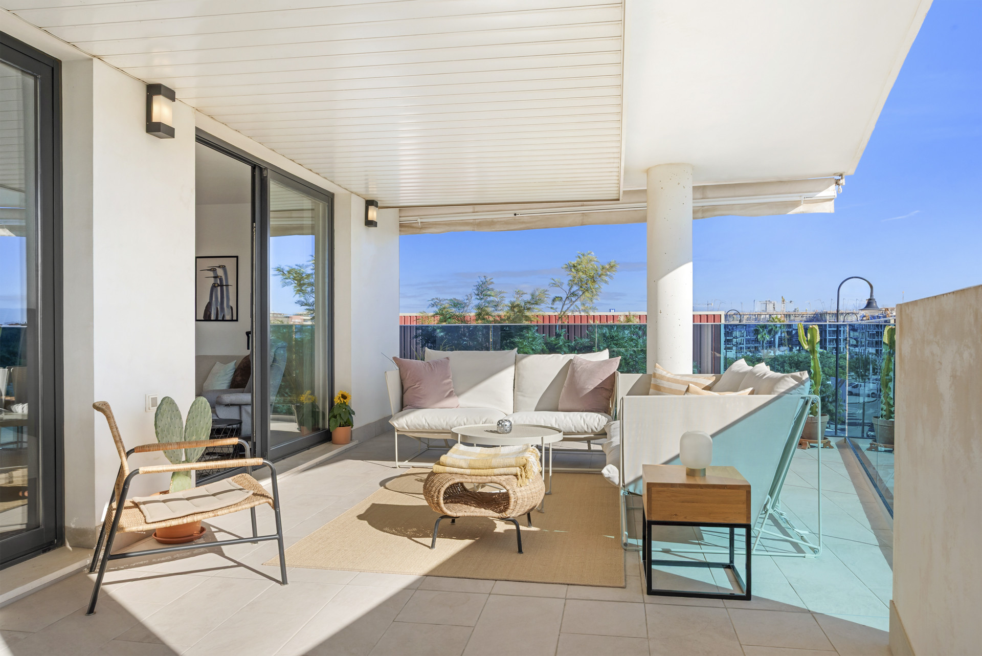 Covered balcony with white sofas and a glass railing, accessed by sliding glass doors from indoors.