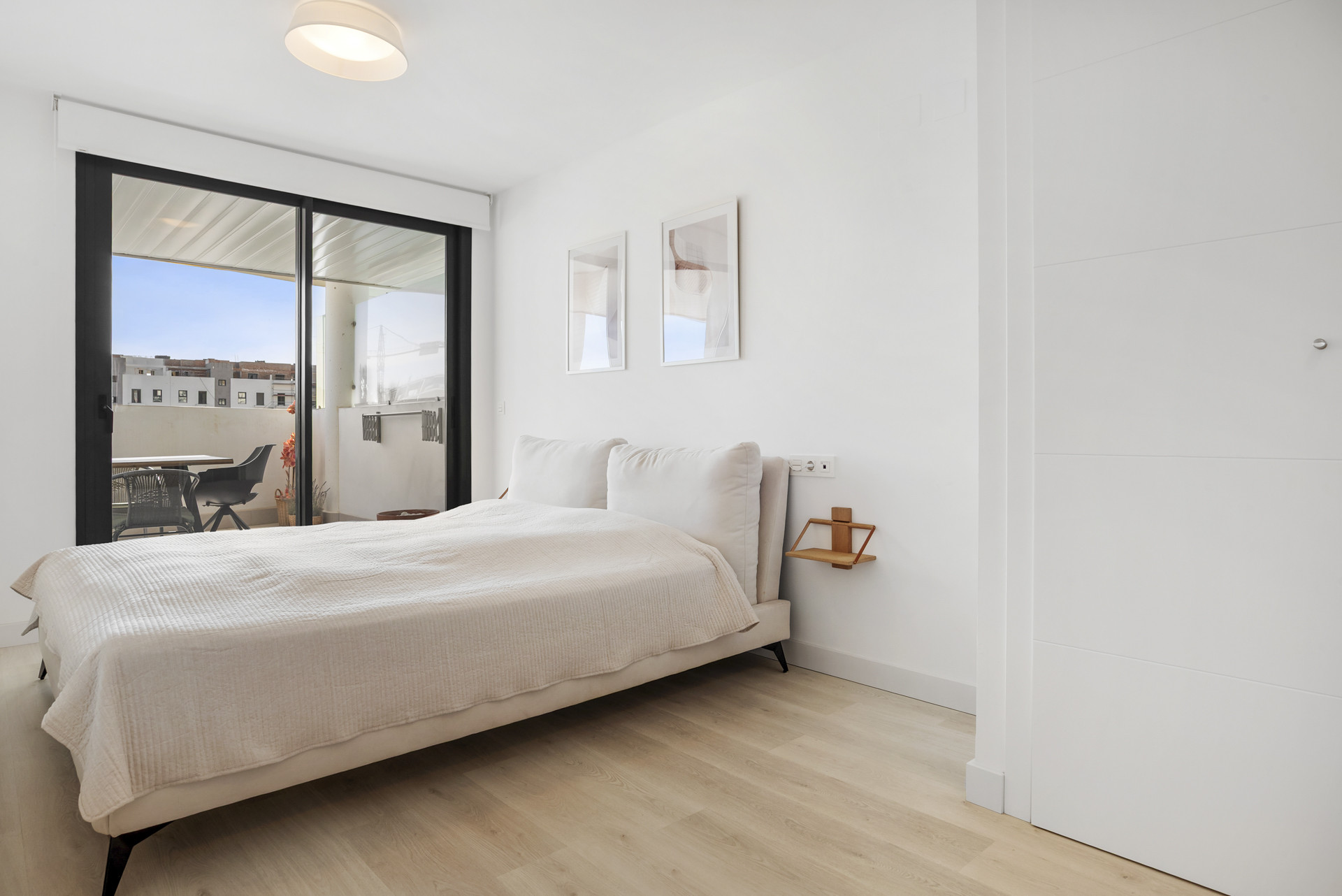 Bedroom with a large bed, two framed pictures, light wood floor, and glass sliding door to a balcony.