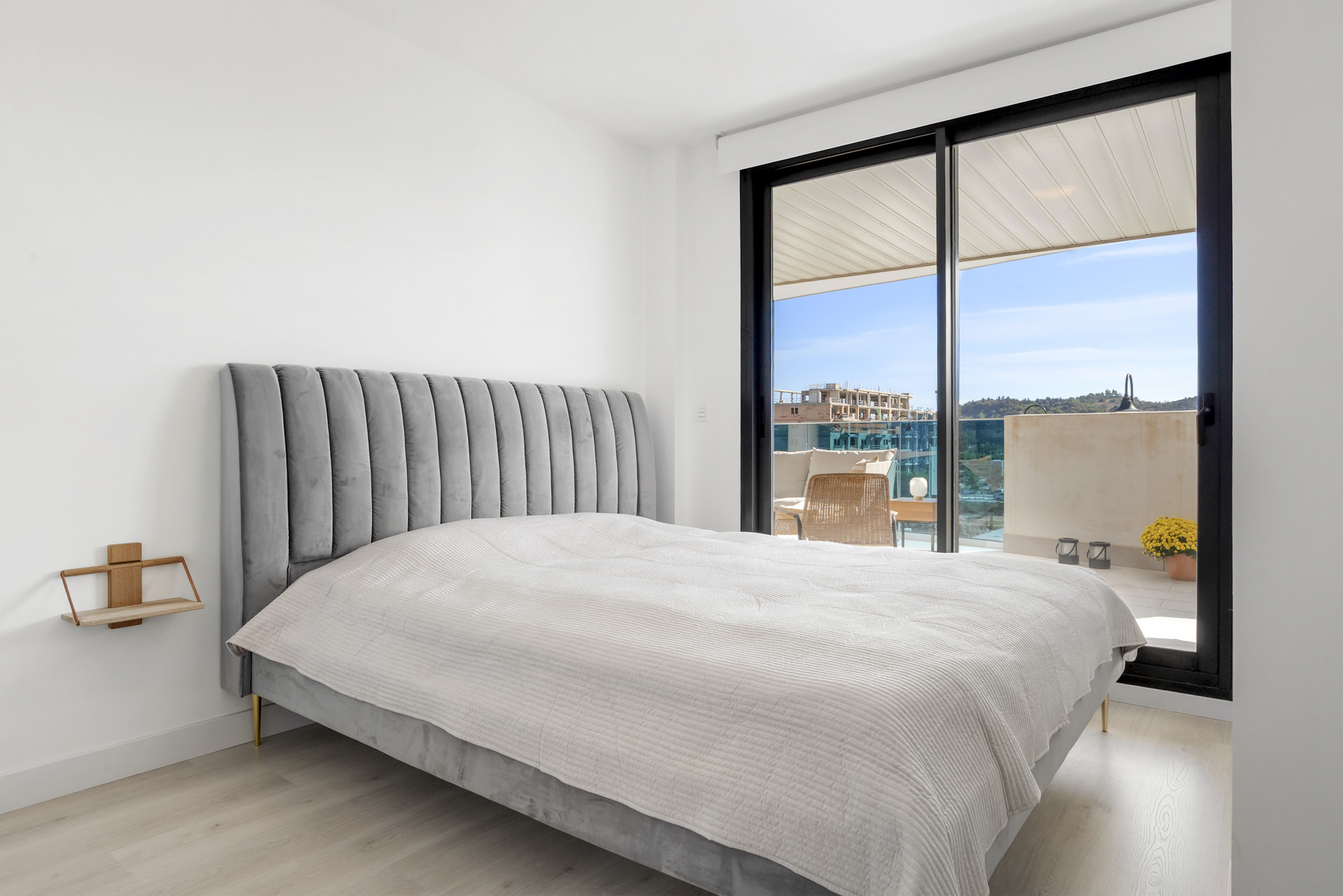 Bedroom with a gray upholstered bed, light wood floor, and a glass sliding door opening to a balcony.