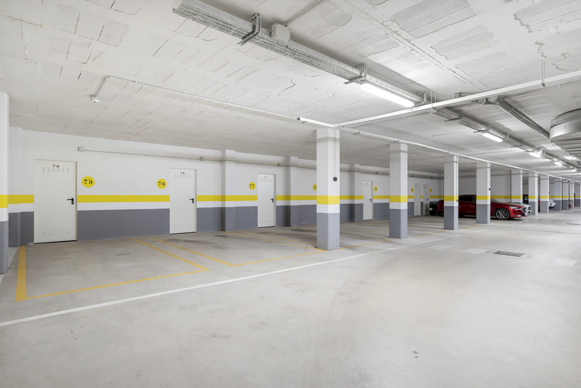 Underground parking garage with numbered storage unit doors, yellow striped walls, and parked cars.