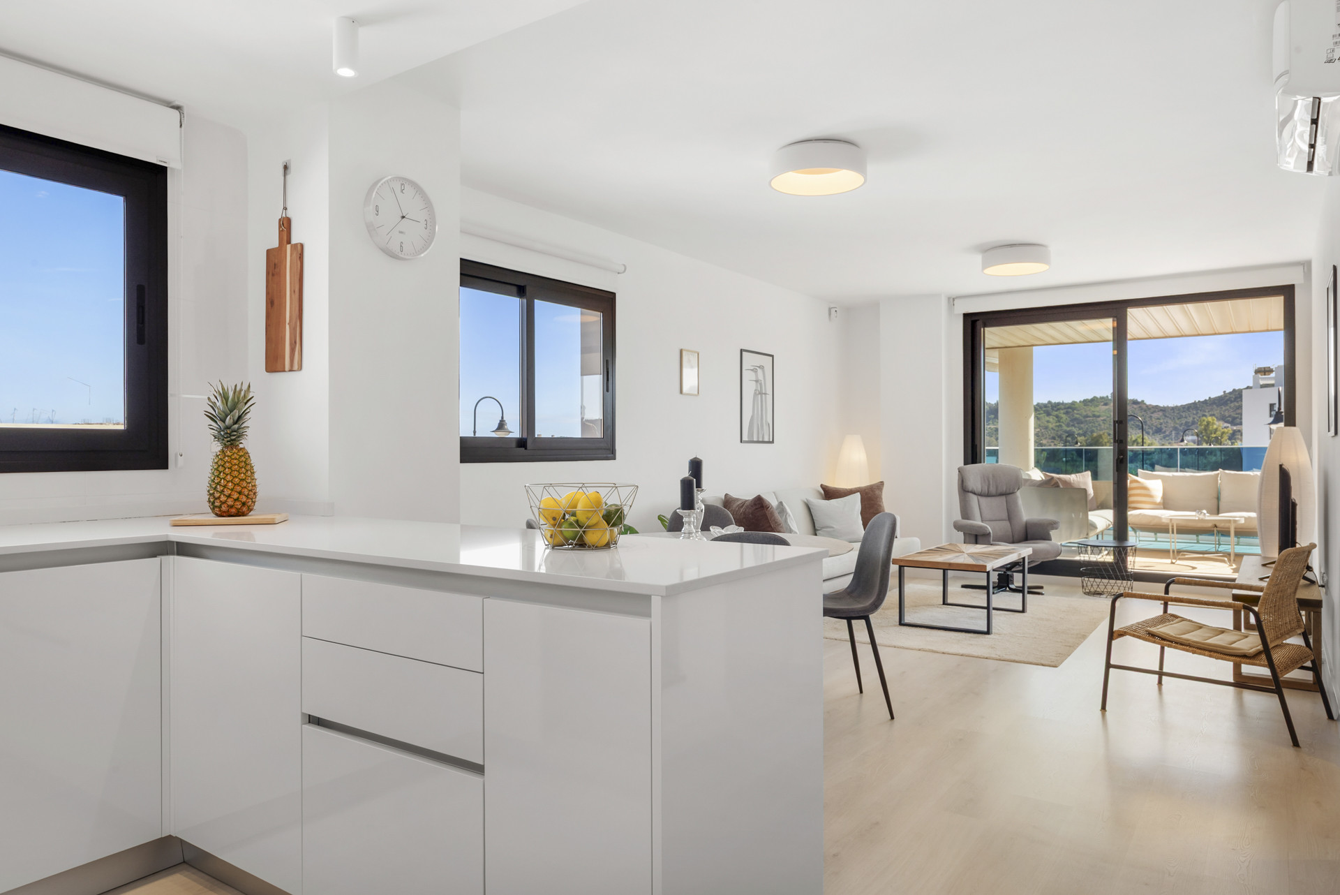 View from kitchen area into a modern living room and open balcony with outdoor seating.