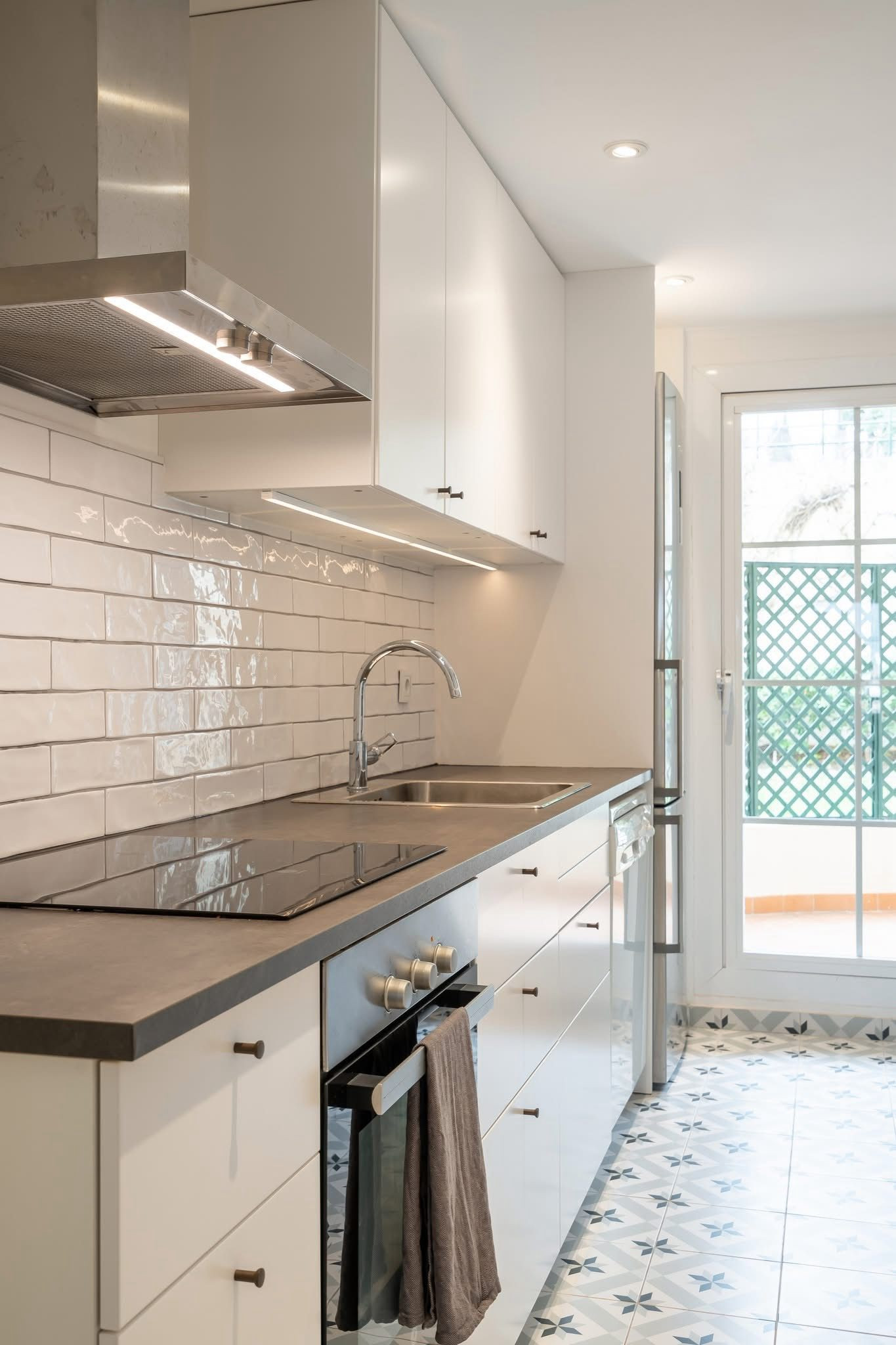 Modern galley kitchen with white cabinets, stainless steel appliances, subway tile backsplash, and patterned floor.