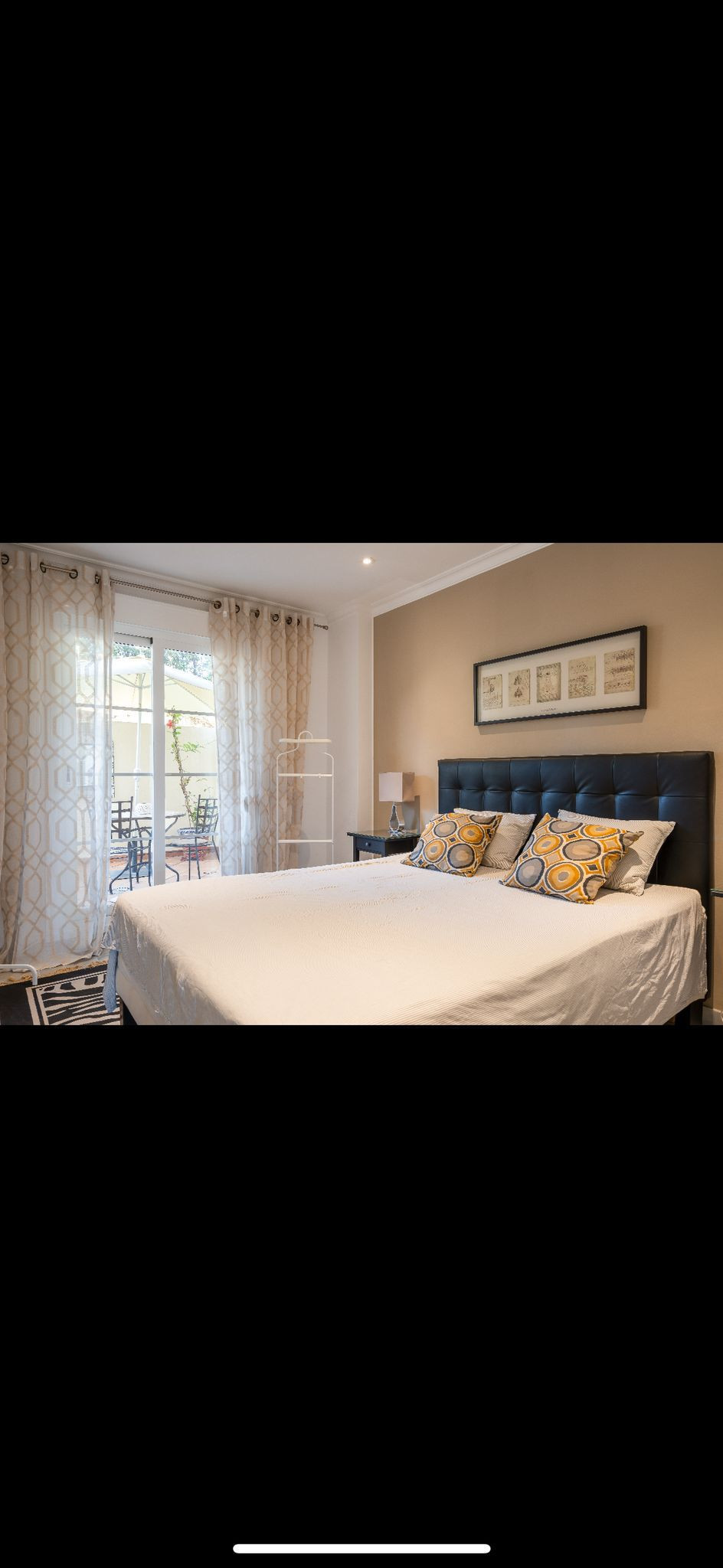 Bedroom with a large bed, dark headboard, two nightstands, and glass doors leading to an outdoor patio.
