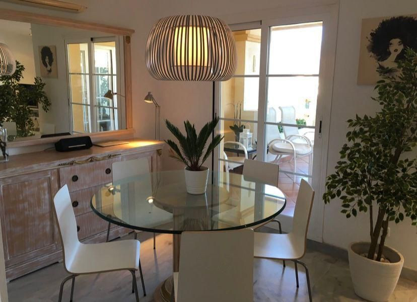 Dining area with a glass table, four white chairs, a wooden credenza, and a large mirror.
