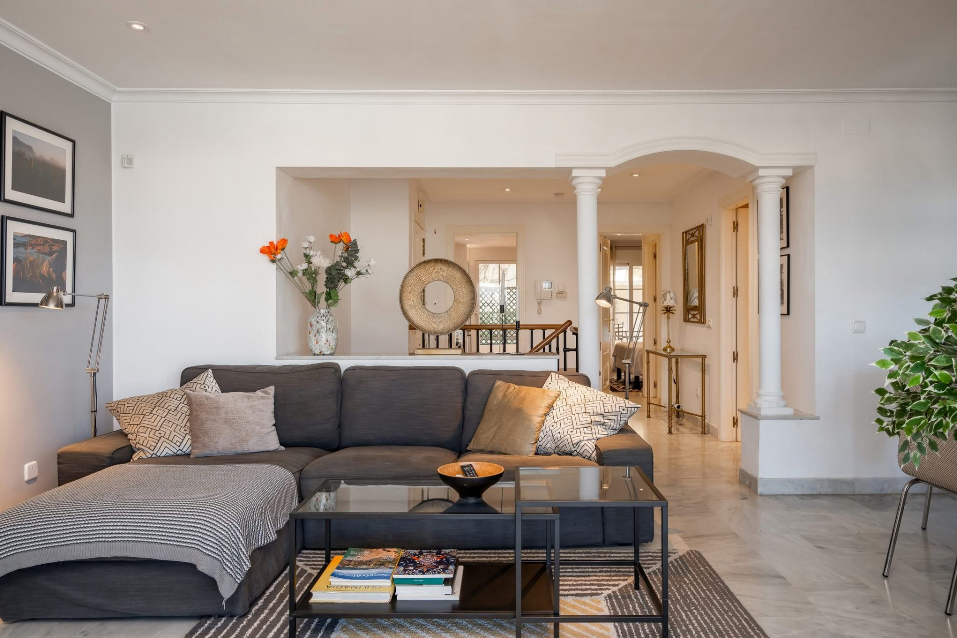 Living room with a gray sectional sofa, glass coffee table, and an arched hallway with columns.