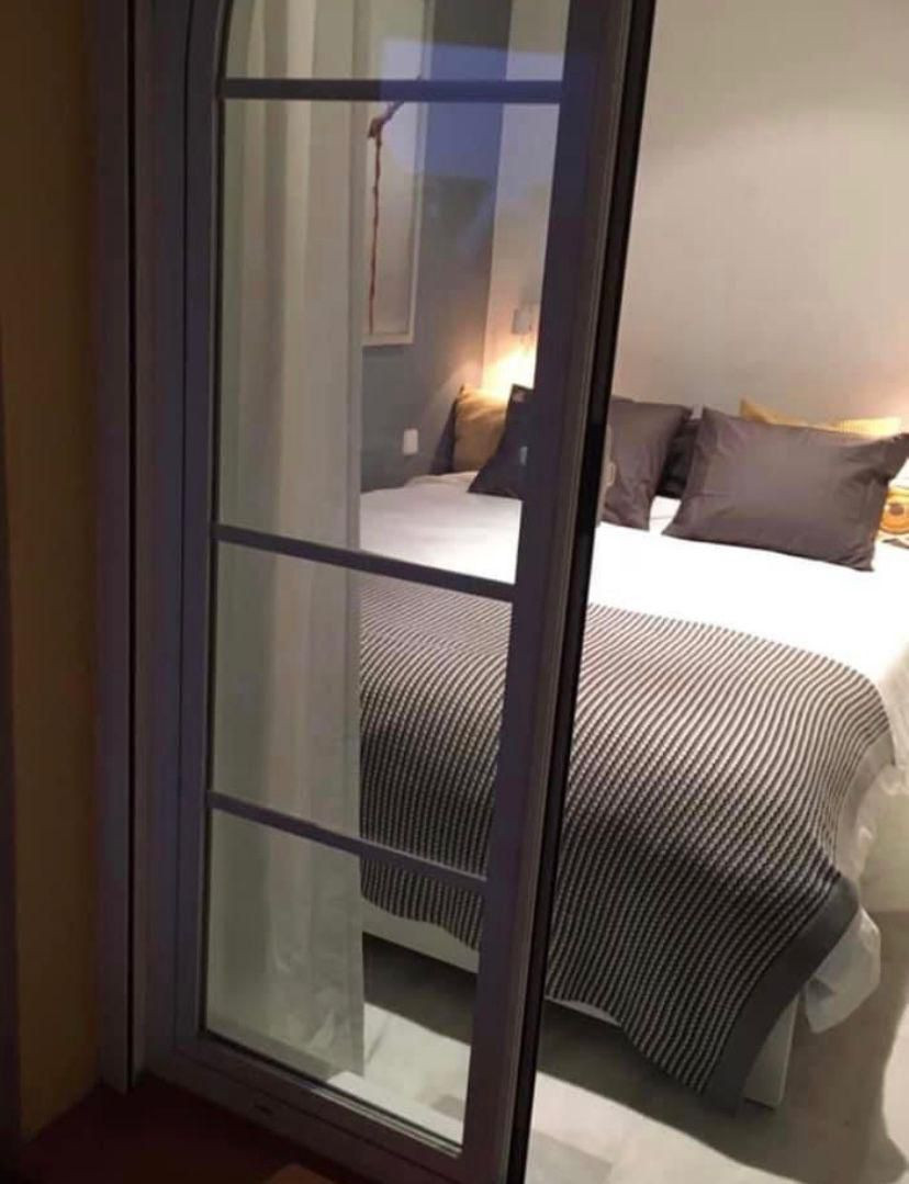 Bedroom with a striped blanket and throw pillows, viewed through a glass door from the hallway.