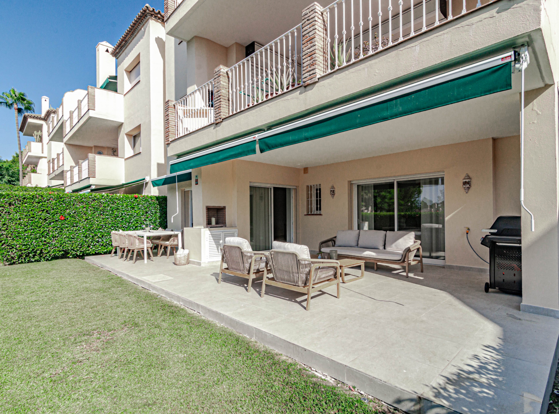Outdoor patio with dining area, lounge seating, sun loungers, grass lawn, and building exterior.