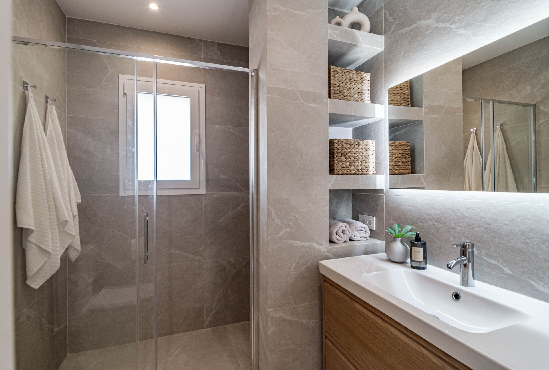 Bathroom with a glass shower, a small window, a vanity with a sink, and recessed shelving.