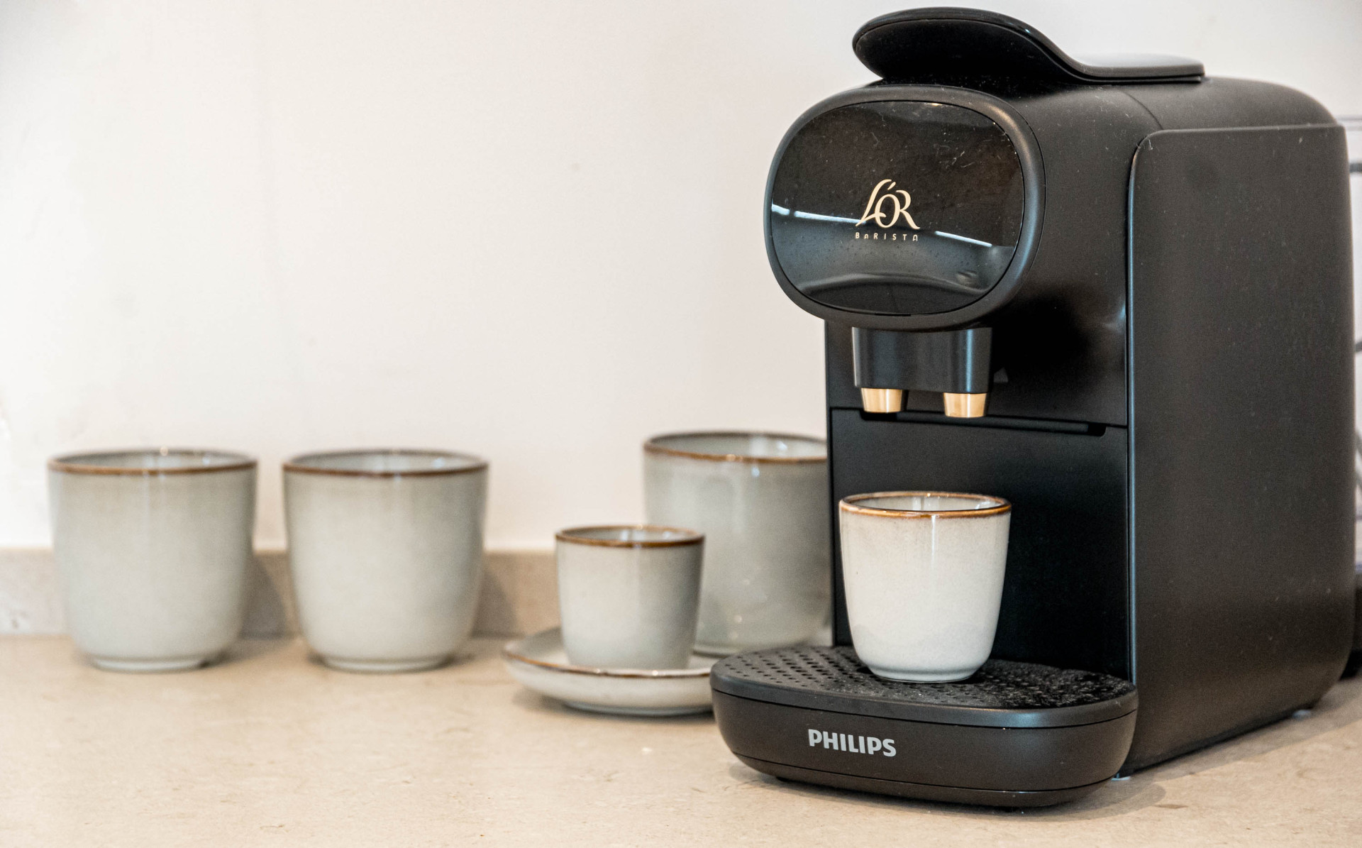 Black coffee machine with cups on a light countertop.