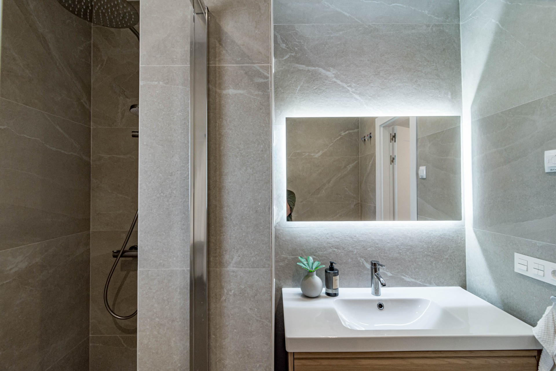 Bathroom vanity with a white sink, light wooden base, and a backlit mirror.