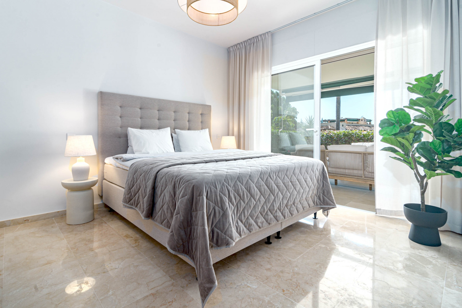 Bright bedroom with a large bed, two nightstands, and glass sliding doors leading to a patio.