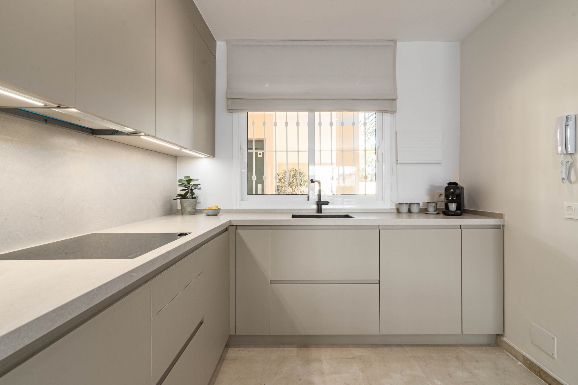 Kitchen with light grey cabinets, black sink and faucet, integrated stovetop, and window overlooking a patio.