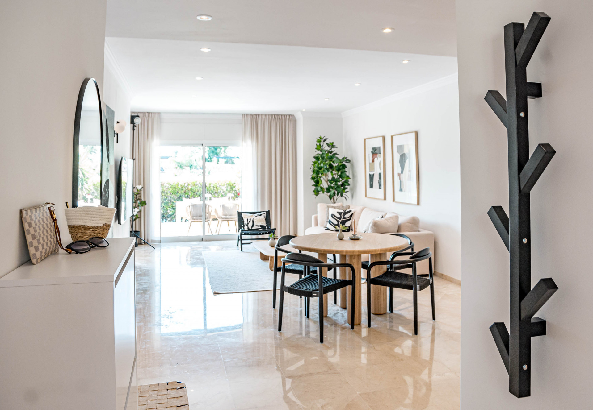 Entryway view of open living and dining area with modern black coat rack and natural light.