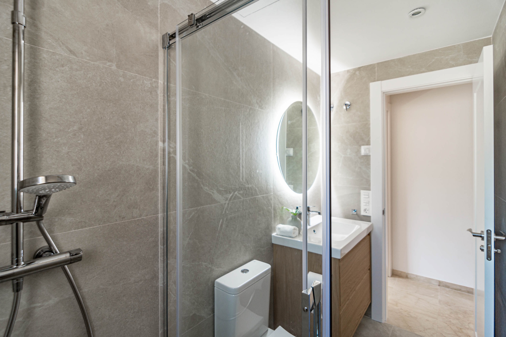Bathroom shower with a view of the vanity, sink, and backlit mirror through the glass panel.