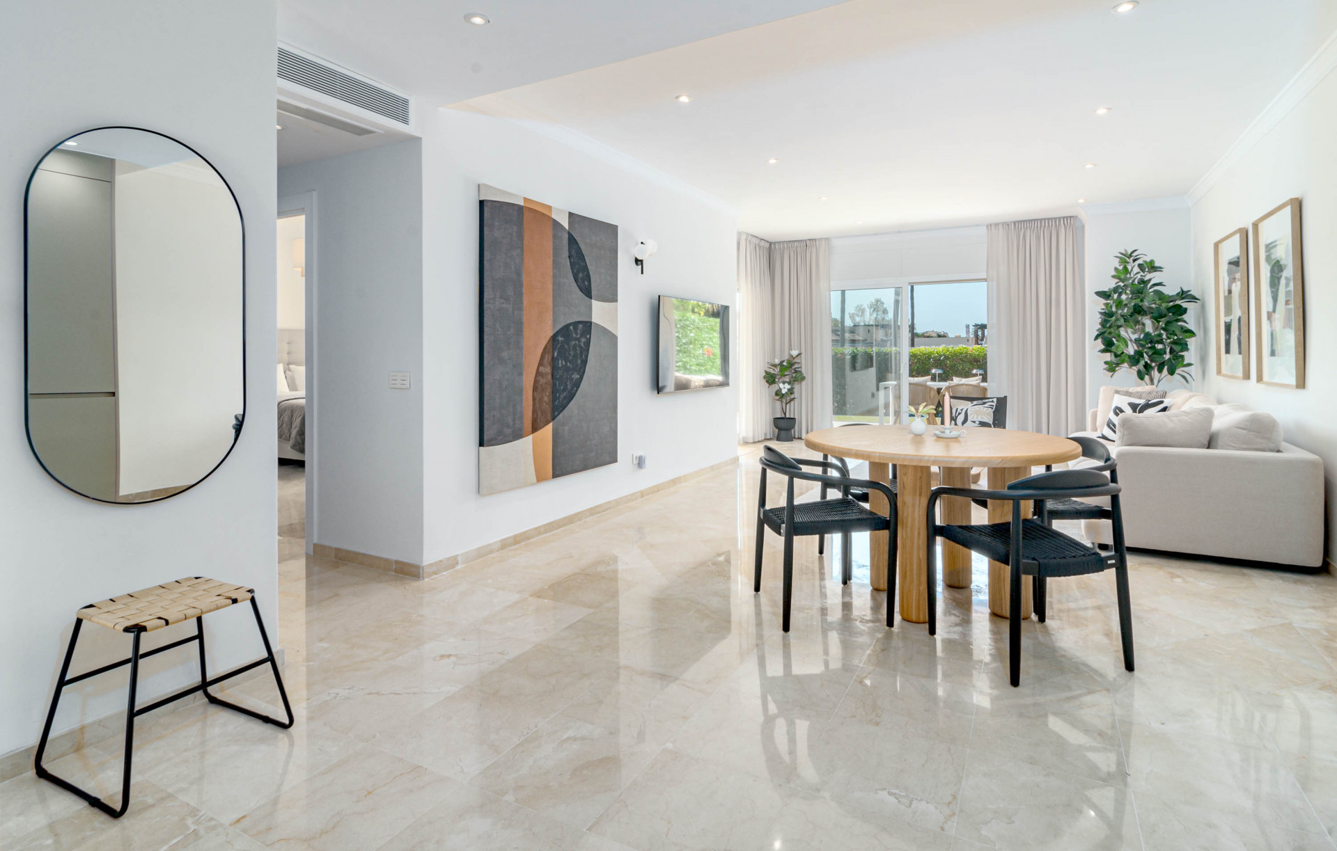 Living and dining area featuring a round wooden table, oval mirror, and large abstract artwork.