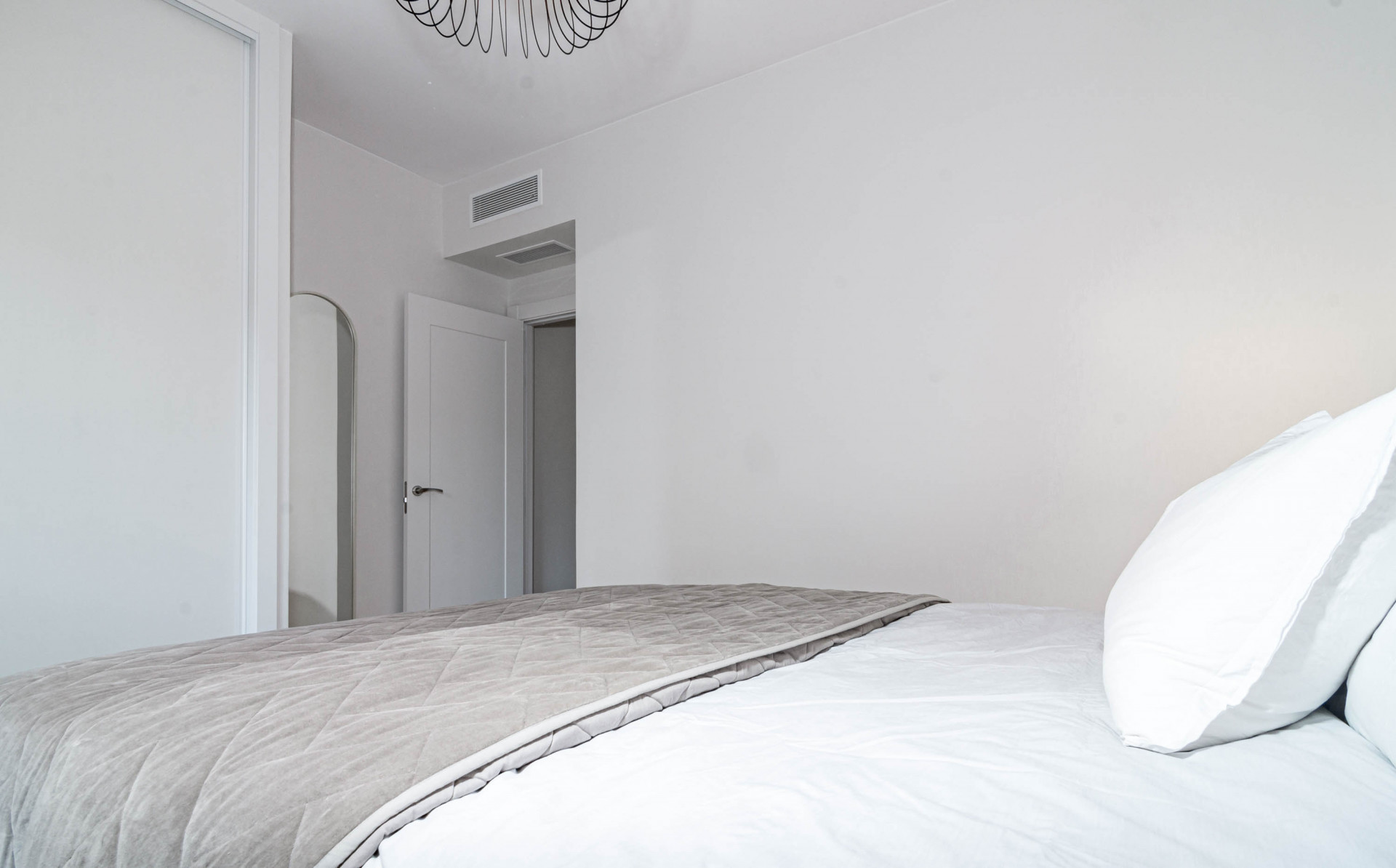 Bedroom view from the bed showing a white wall, a closed door, and a partially visible mirror.