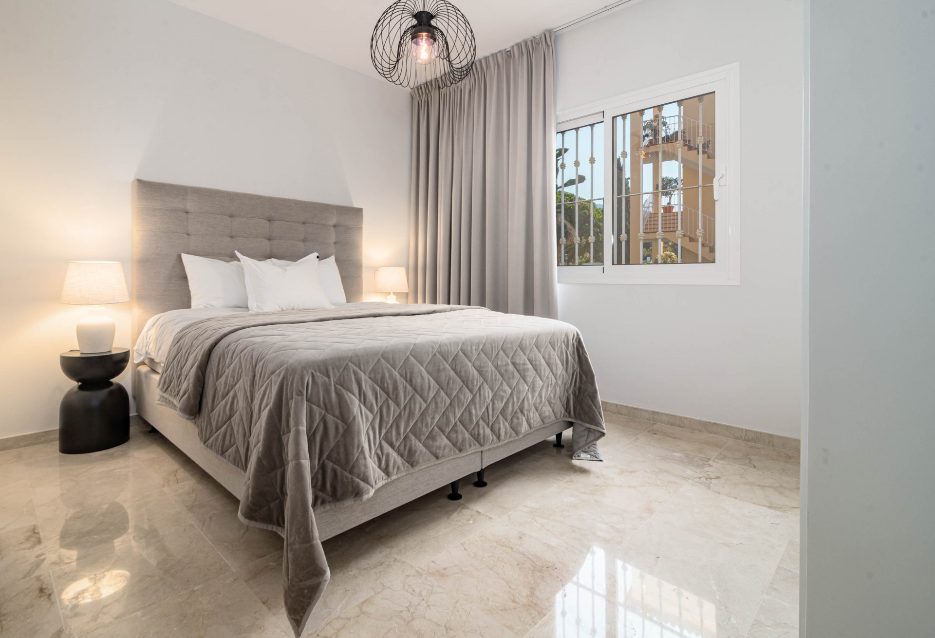 Bedroom with a bed, two nightstands, a hanging light fixture, and a window with security bars.