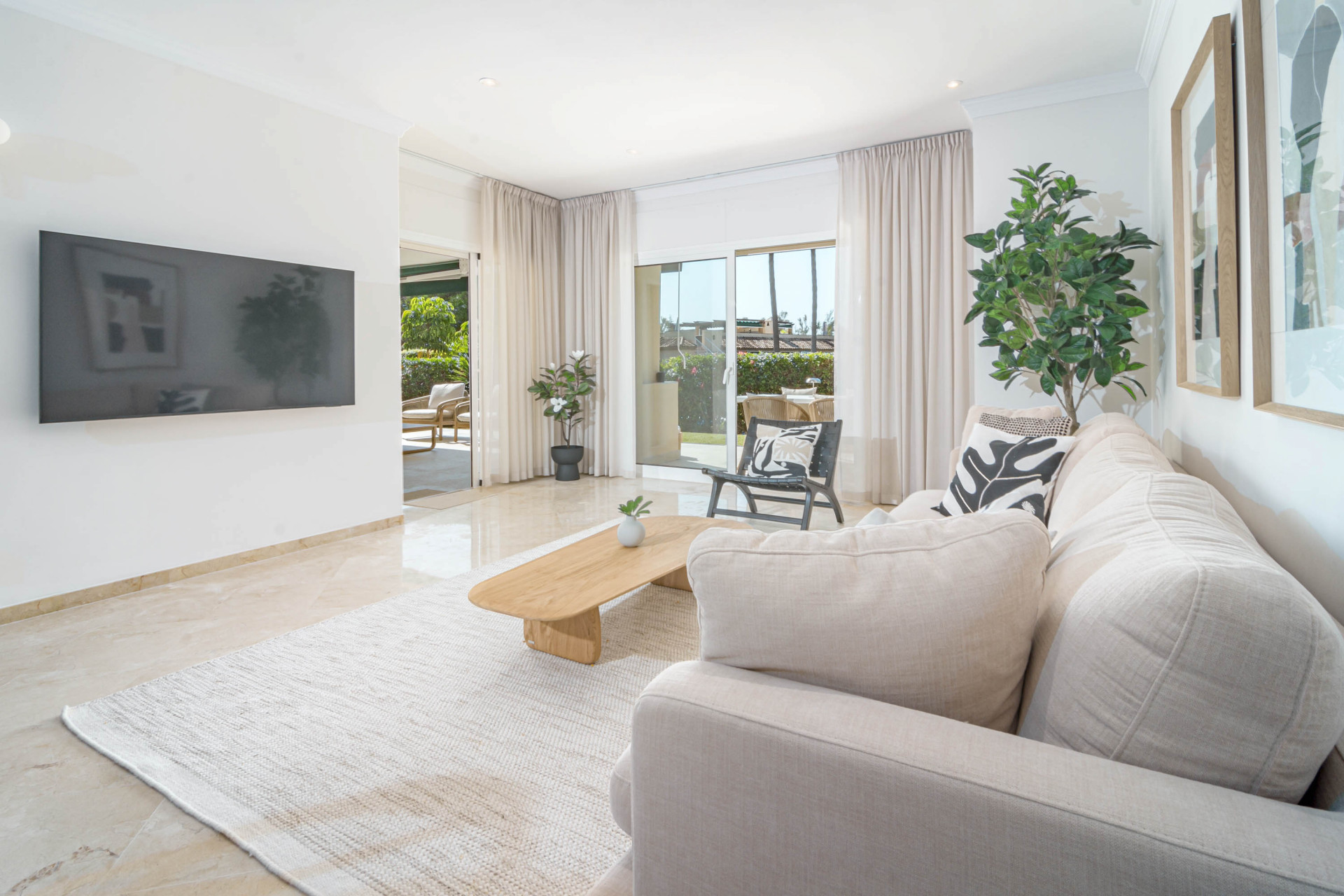 Living room from sofa side showing a wall-mounted TV, beige sofa, and sliding doors to the exterior.