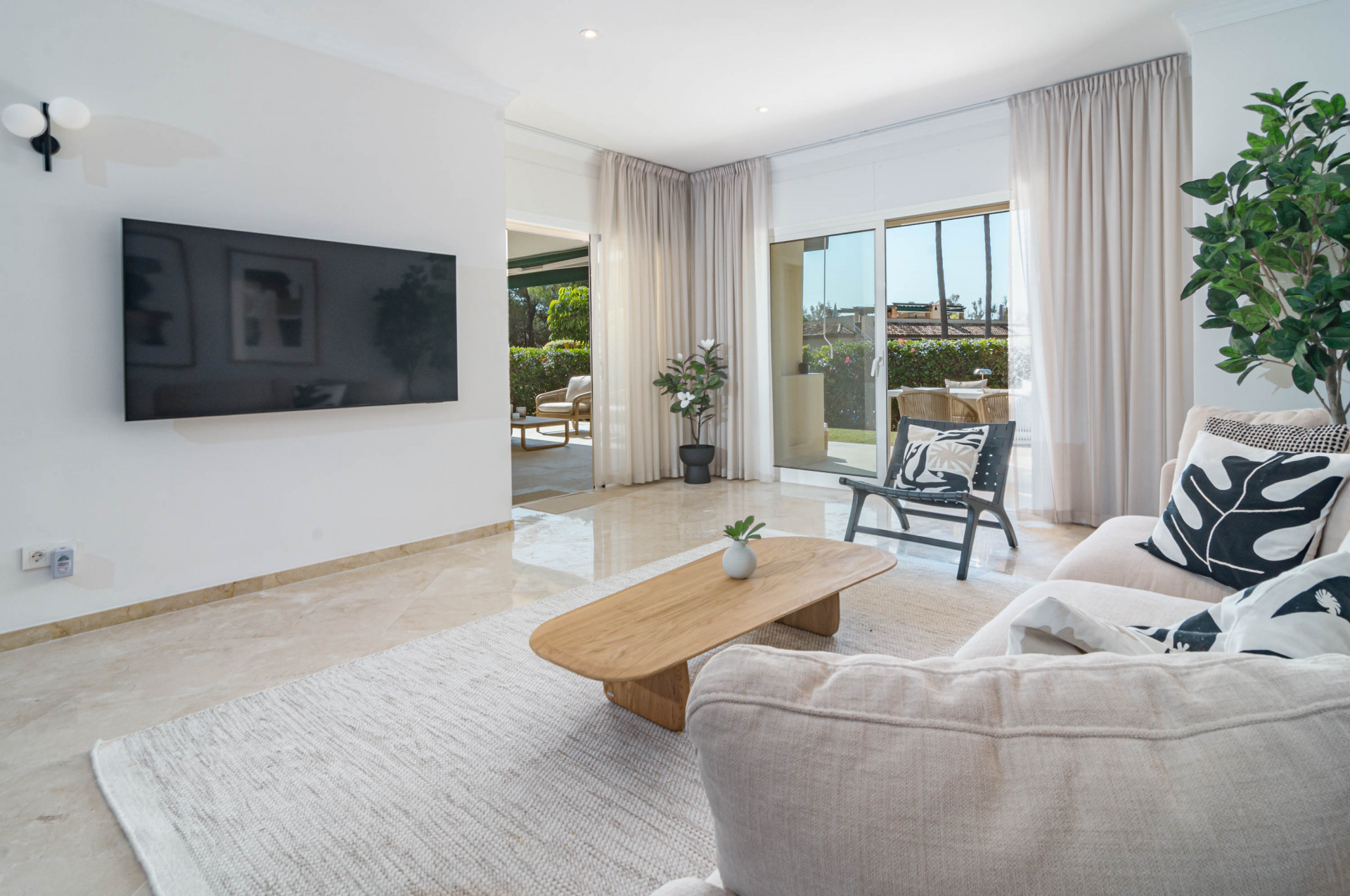 Living room looking towards exterior. Wall-mounted TV, light sofa, and black lounge chair visible.