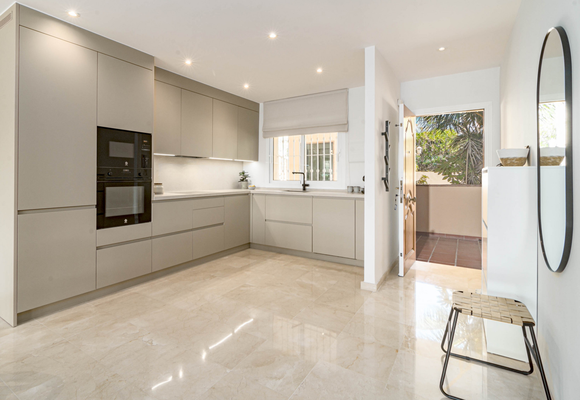 Bright kitchen with light cabinetry, black oven, and an open doorway leading to an outdoor space.