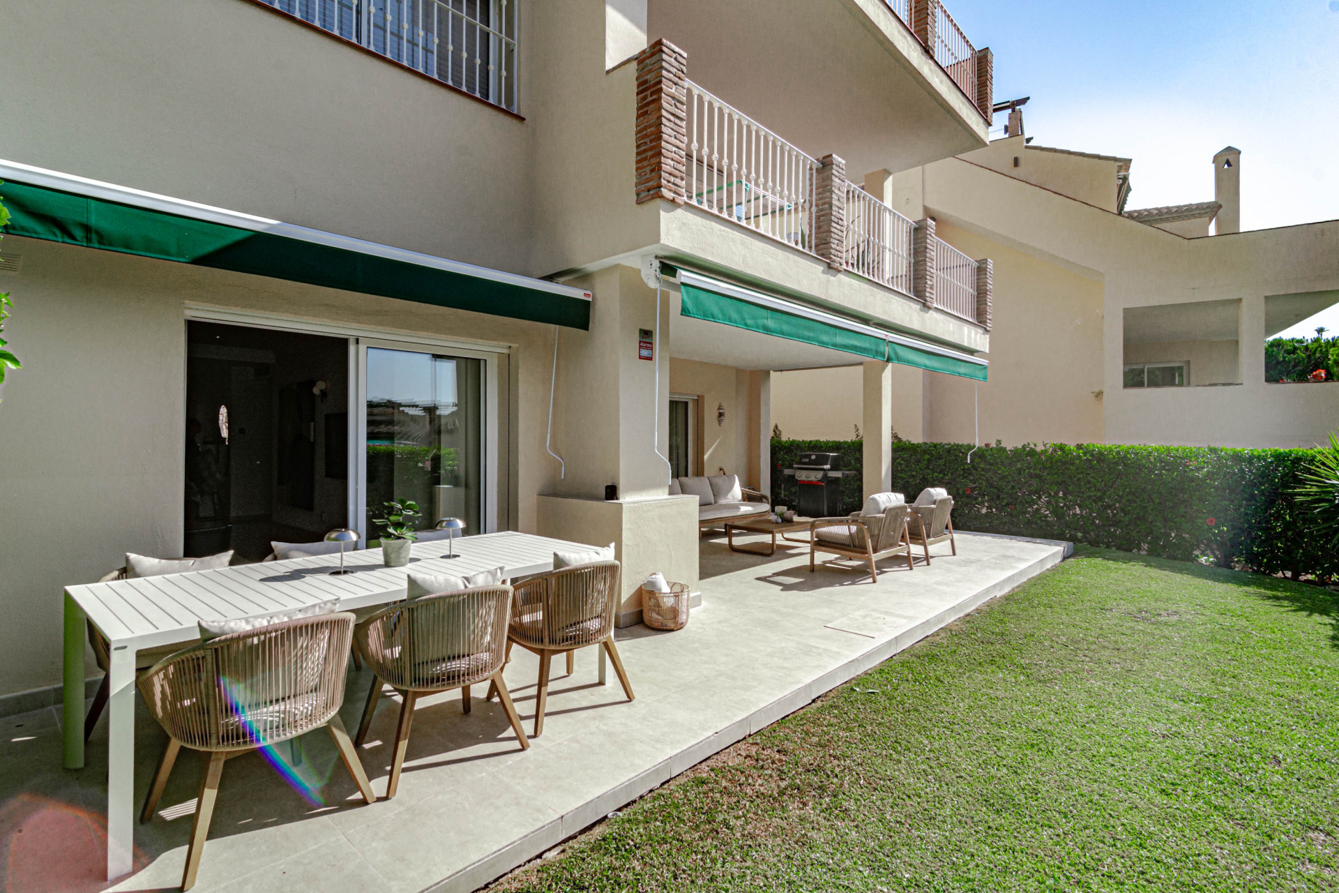 Lawn and patio with outdoor dining table, lounge chairs, awnings, and apartment building facade.