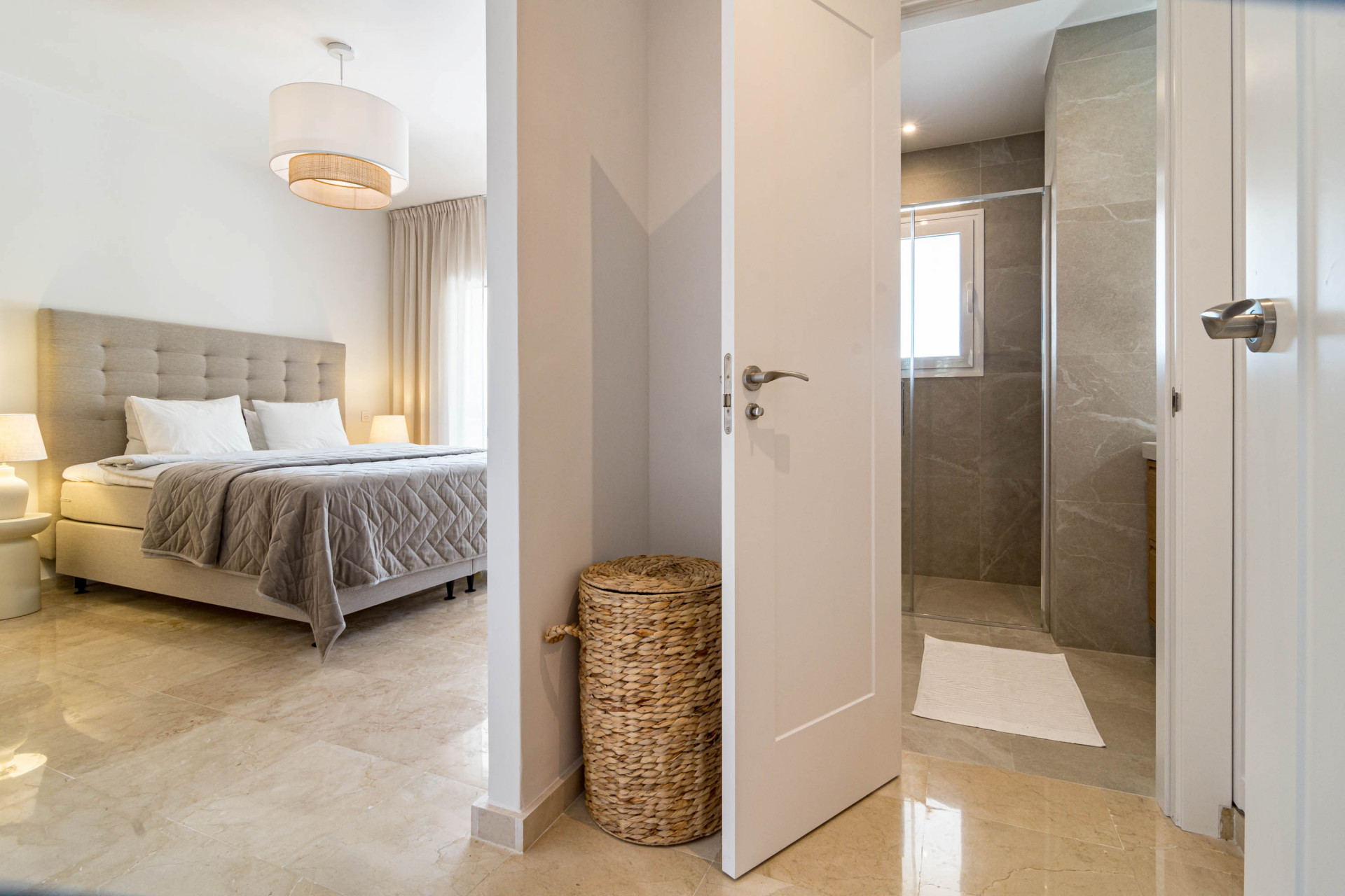 Bedroom with a large bed and a glimpse into a modern bathroom through an open doorway.